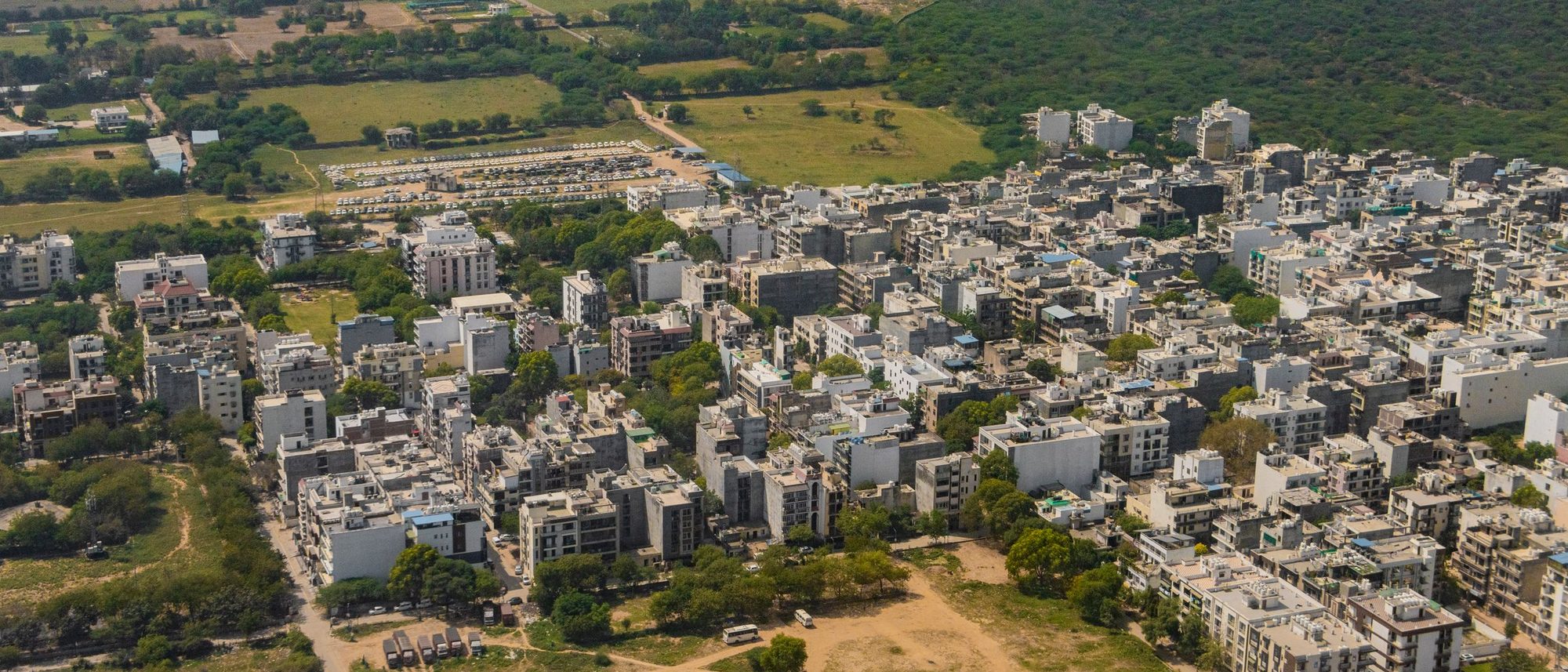 An aerial view of Gurugram’s towers and roads with green land beyond.