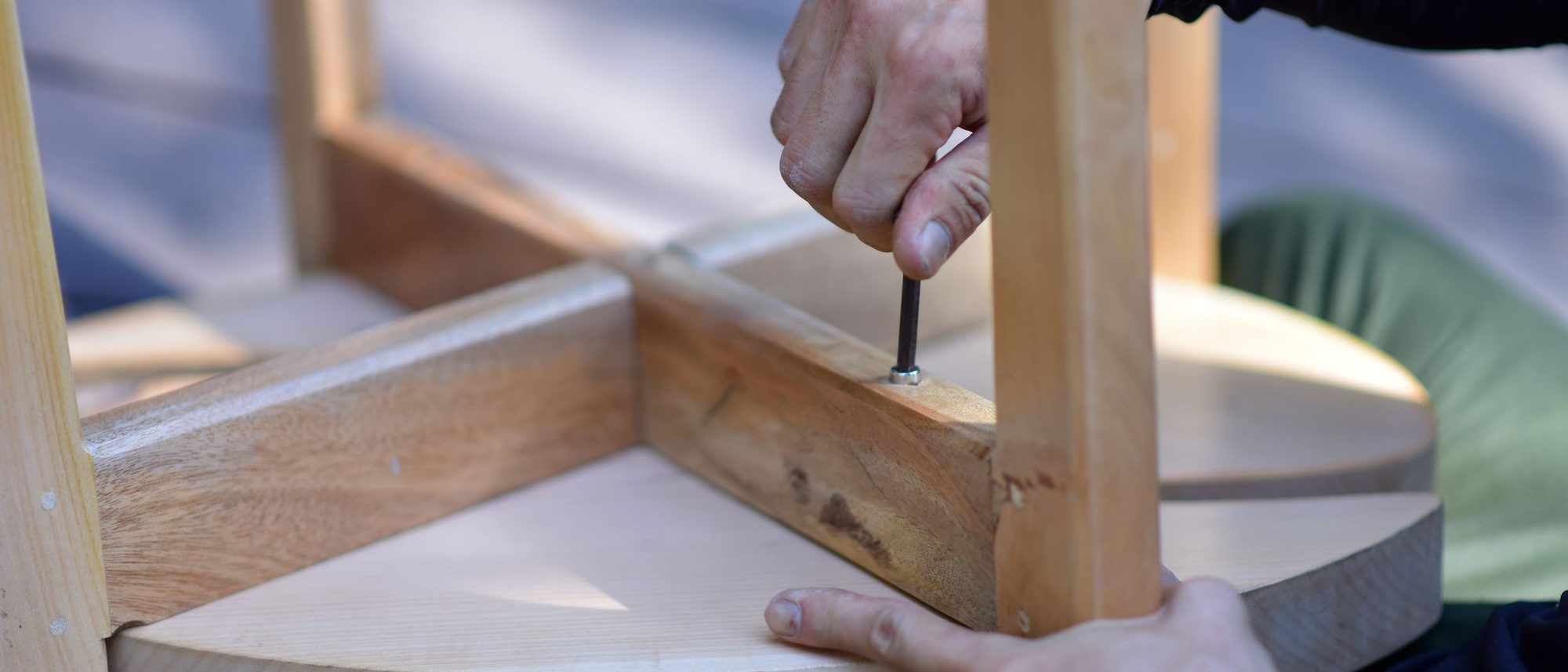 Hands fixing a wooden leg into the frame of a stool.