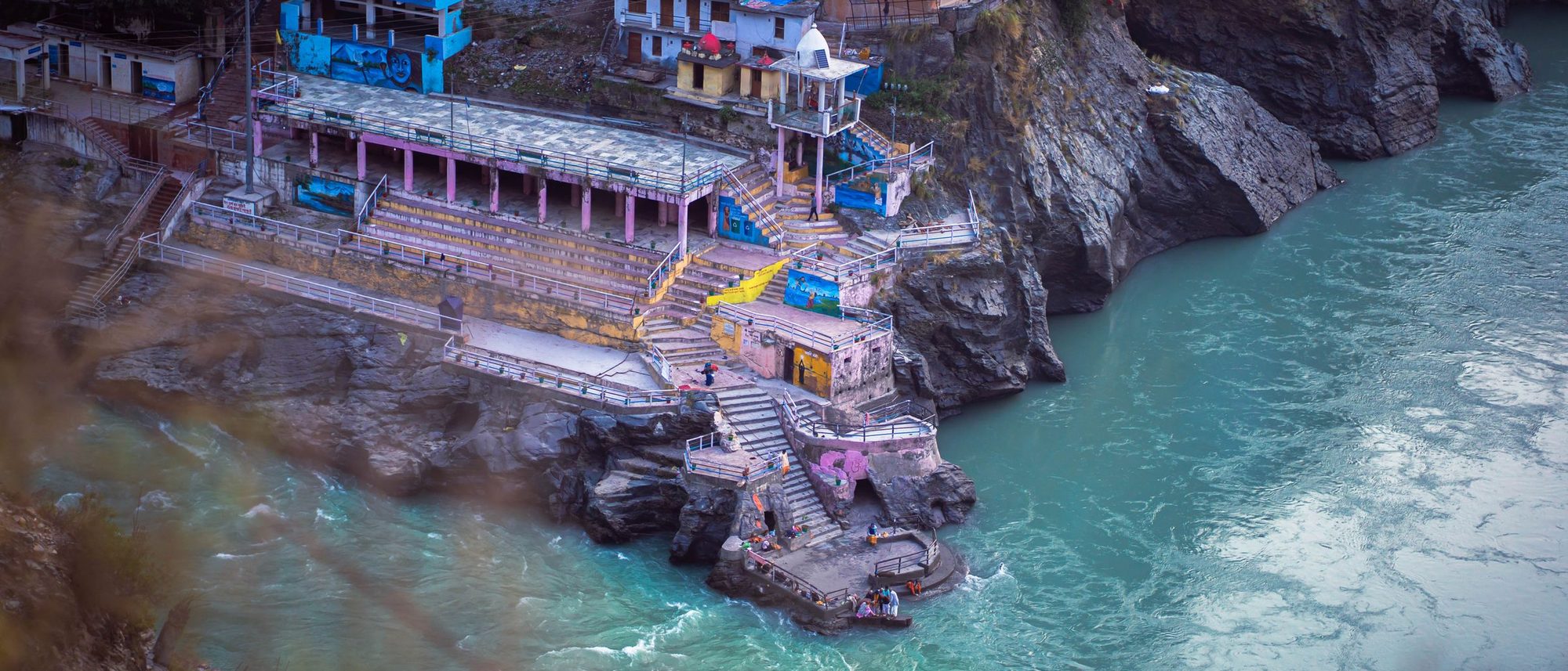 An aerial view of Devprayag in Uttarakhand where two rivers meet among village houses and green hills.