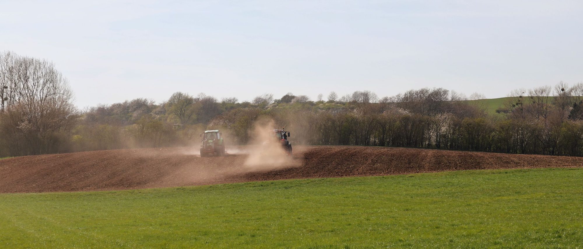A tractor ploughing a wide field under a clear blue sky.