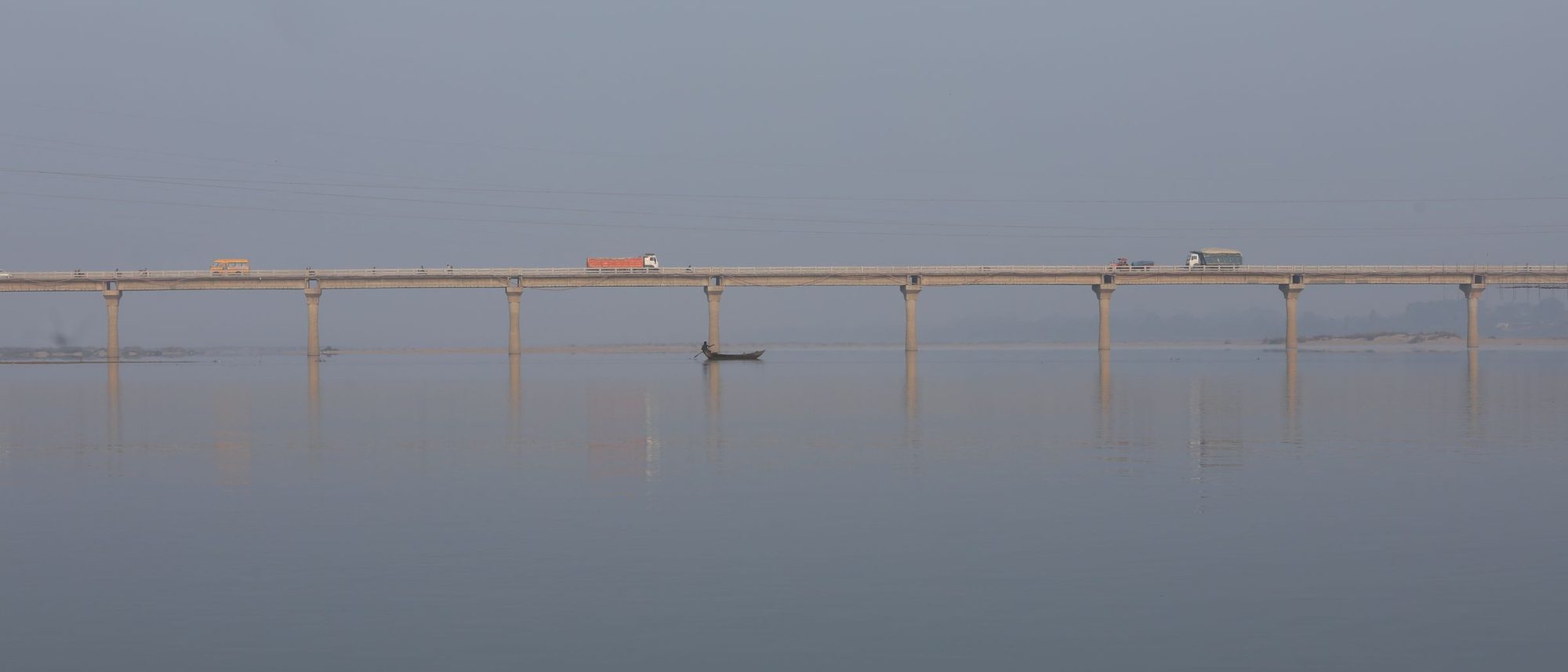 A long bridge crosses a calm river in fog near Chandrapur, its piers reflected in the water.