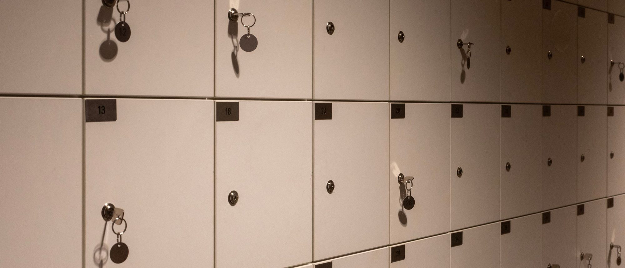 Rows of metal lockers with keys in their doors form a grid in a dim corridor.