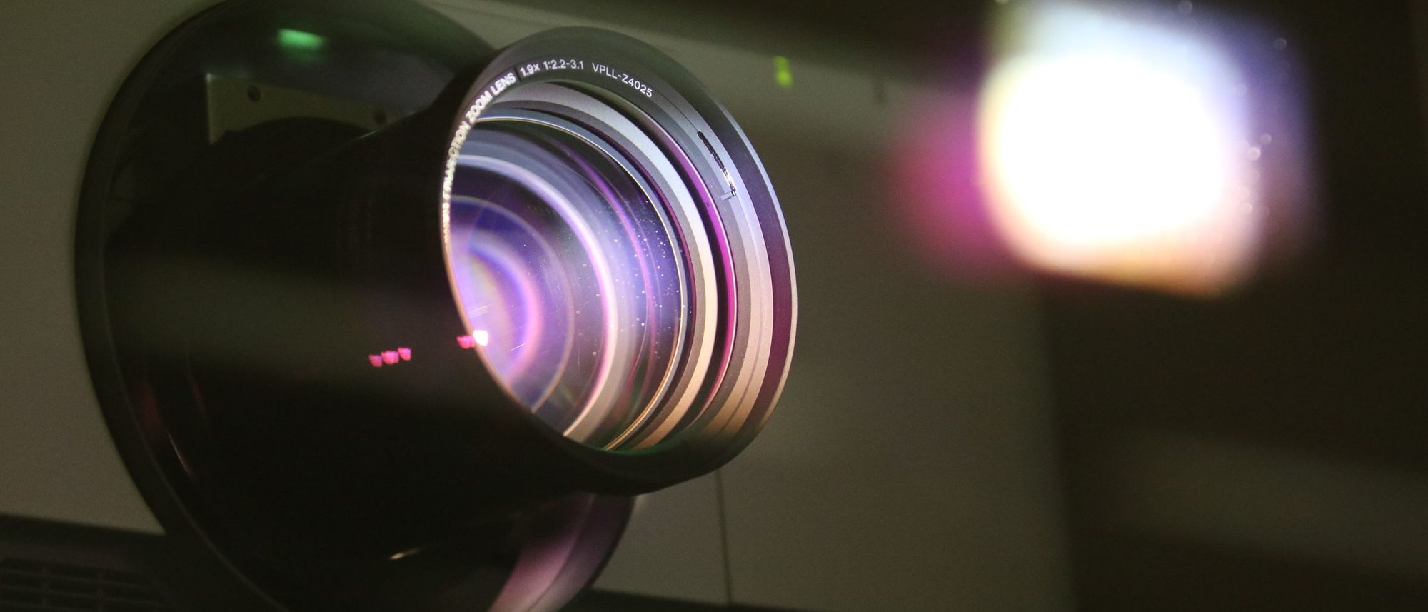 A projector lens throwing a beam of light in a dark room.