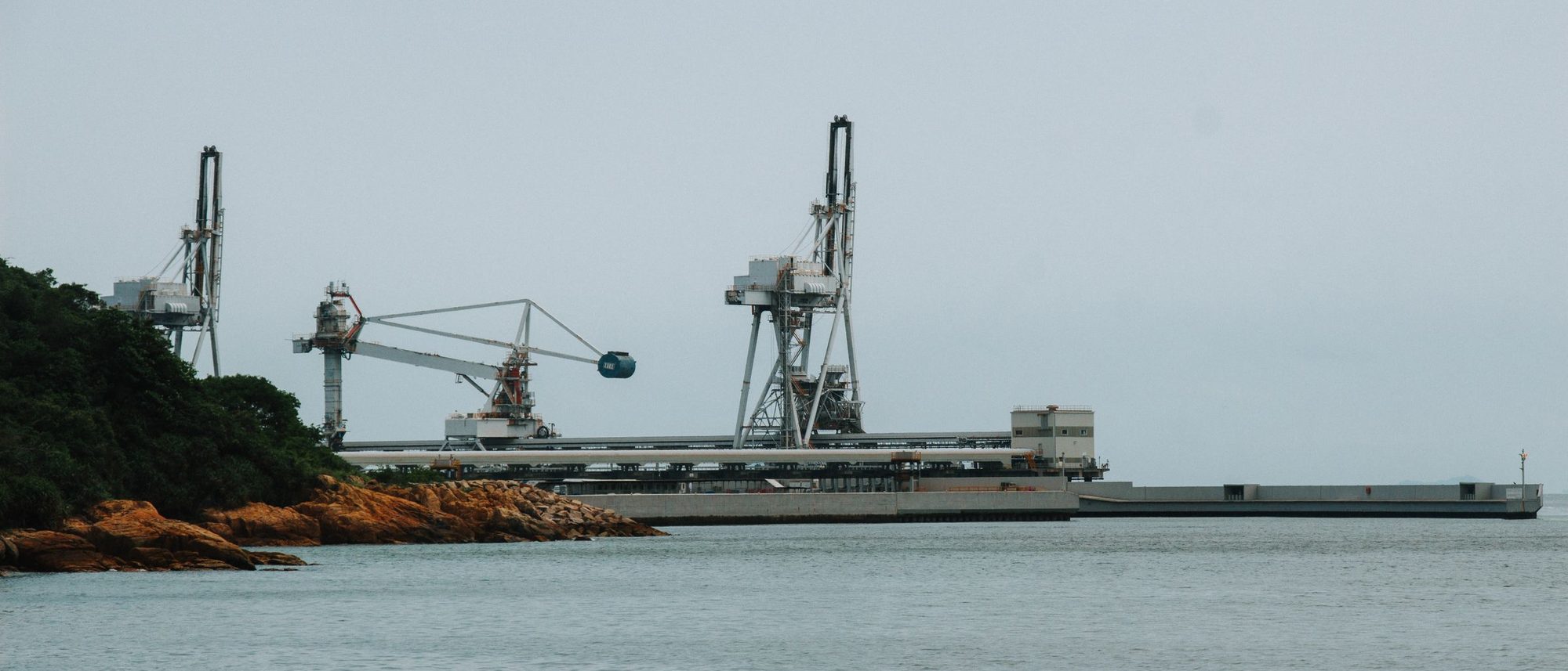 Cranes stand over a quiet dock on an industrial harbour.