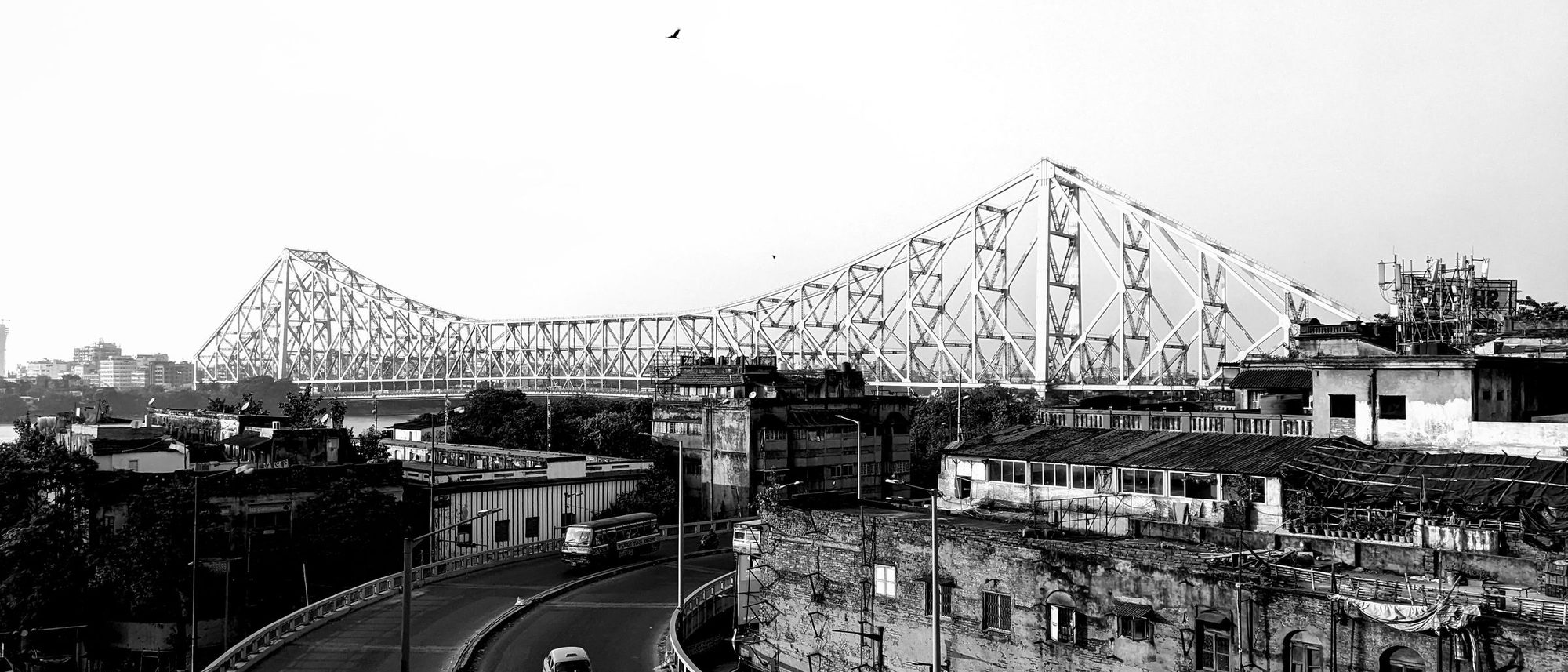 Howrah Bridge spans the river above the Kolkata cityscape in black and white.
