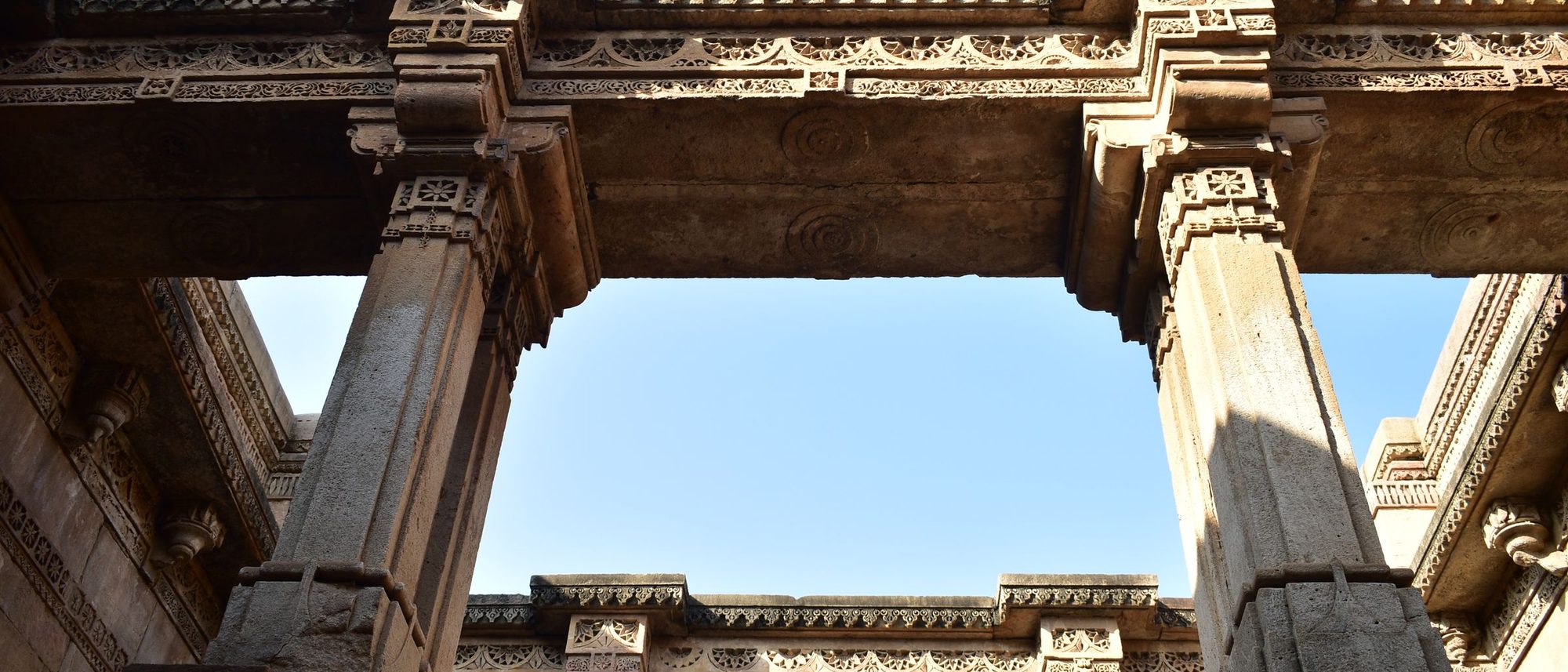 A low-angle view of the carved stone galleries of the Adalaj stepwell in Gujarat under a clear blue sky.
