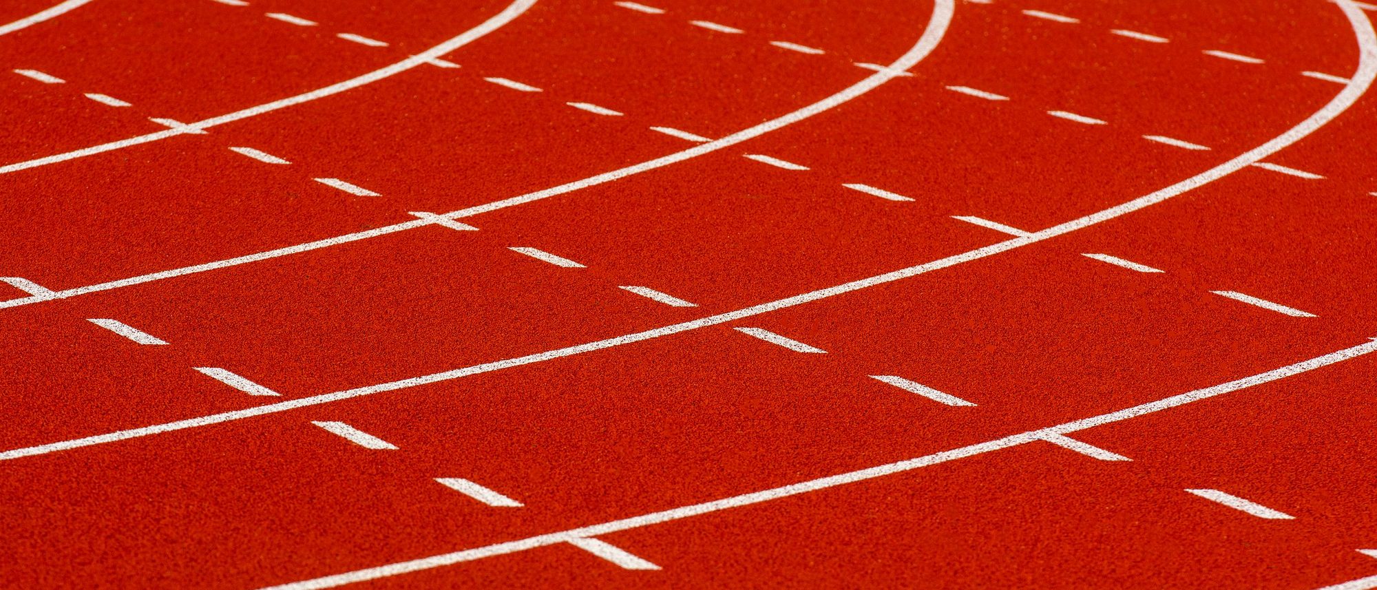 The curve of a red running track with white lane lines.