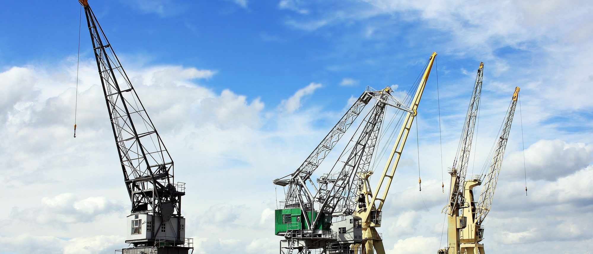 Tower cranes reaching into a blue sky with scattered clouds.