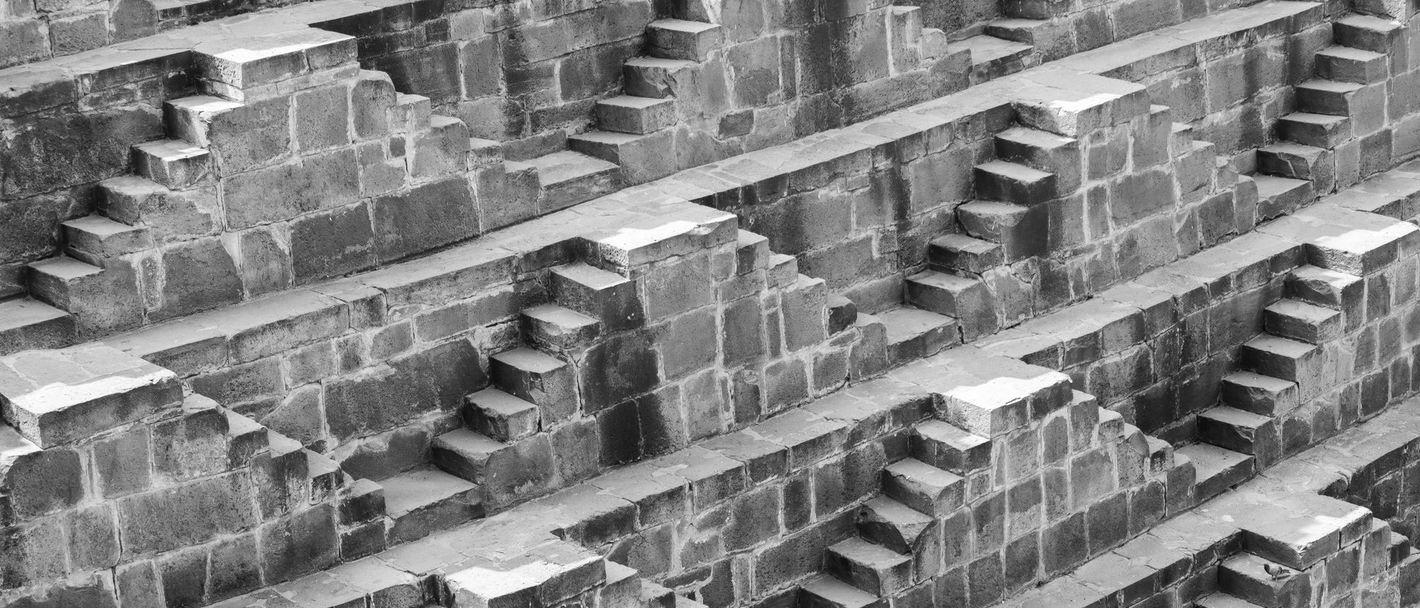 Stone stairways descend in layers down the walls of a stepwell in Bandikui in black and white.