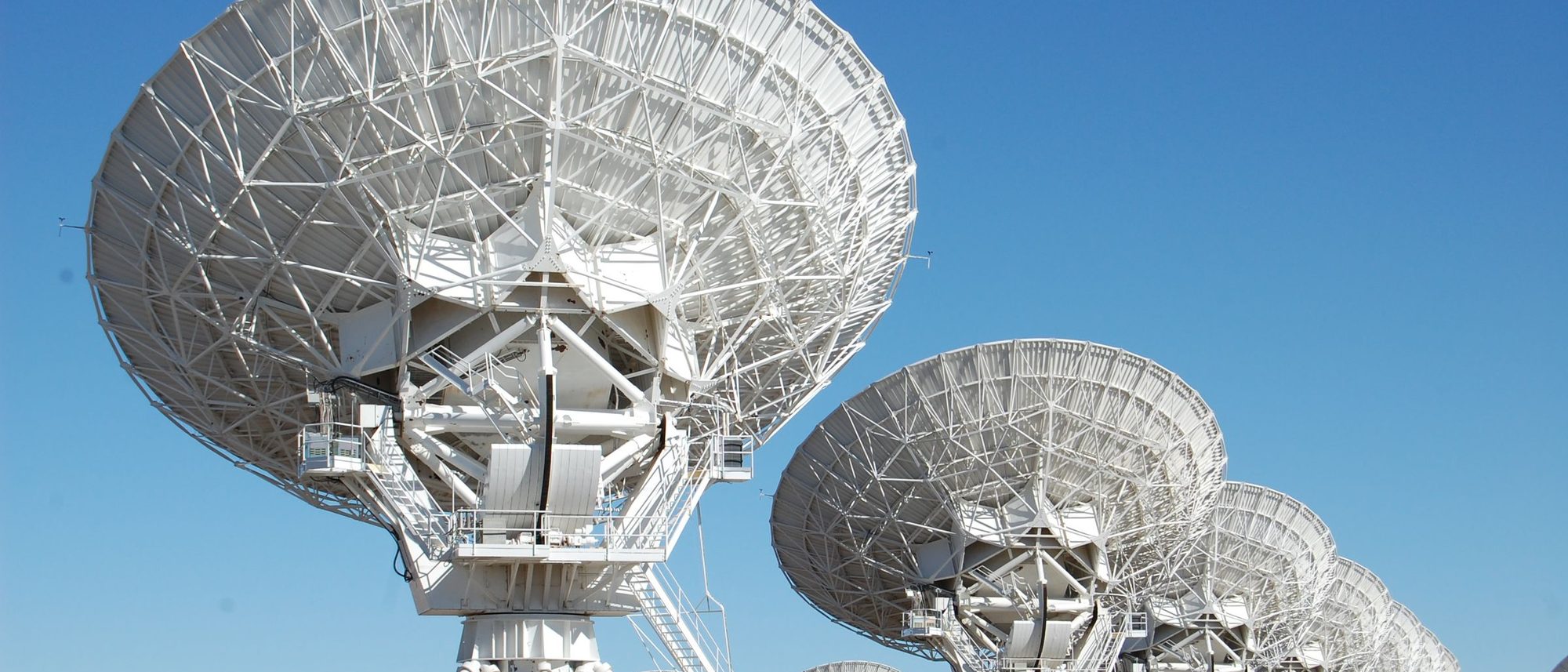 Radio telescope dishes of the Very Large Array in New Mexico stand under a clear blue sky.