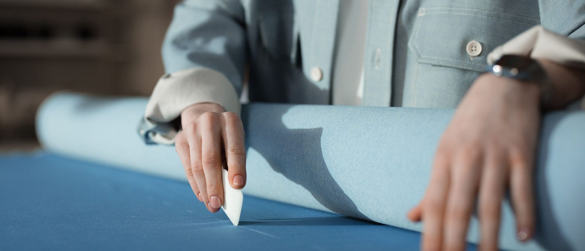 A tailor's hands mark blue fabric with chalk on a cutting table.