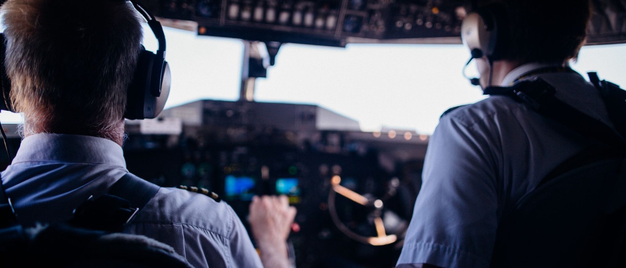 Two pilots seen from behind at the controls of an airliner during take-off.