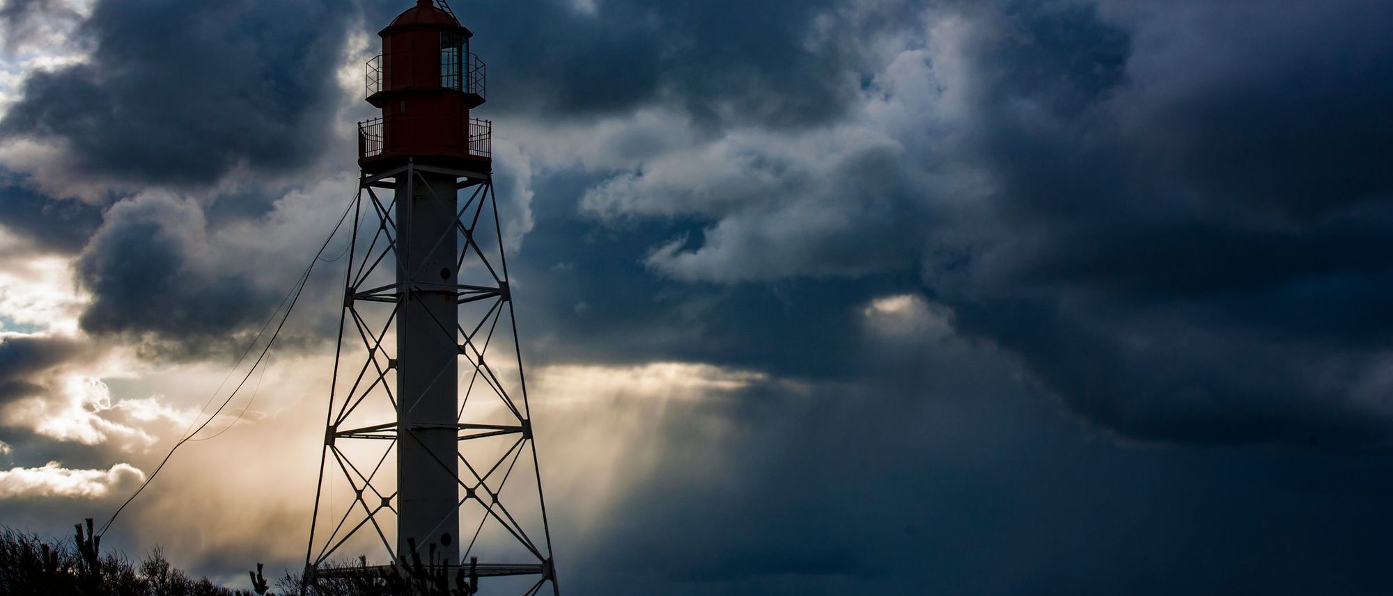 A lighthouse on a low coast beneath a dark storm cloud over the sea.
