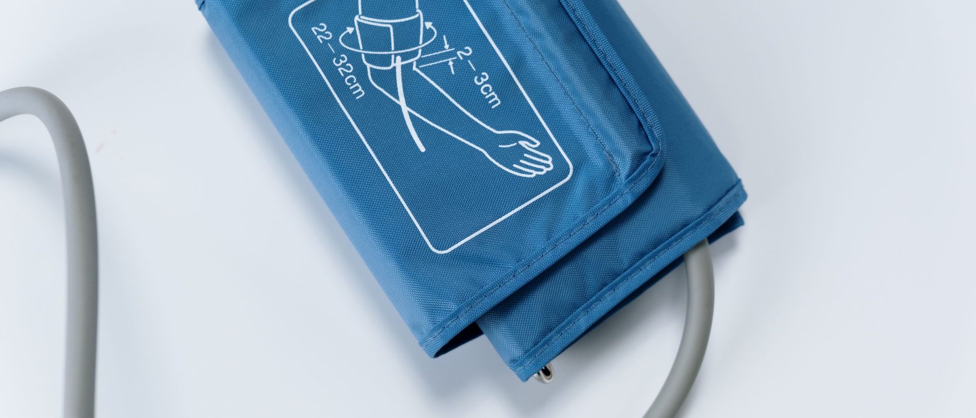 A blue blood pressure cuff and gauge lying on a white surface.