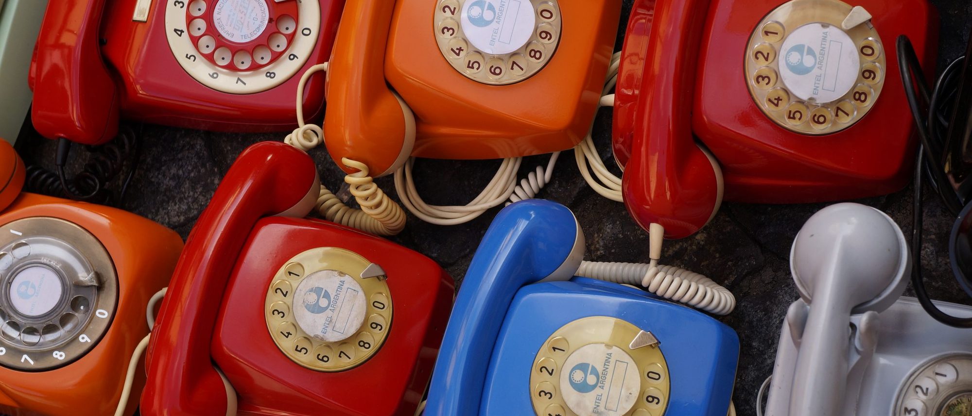 Rotary telephones in red, orange, blue and grey piled together.
