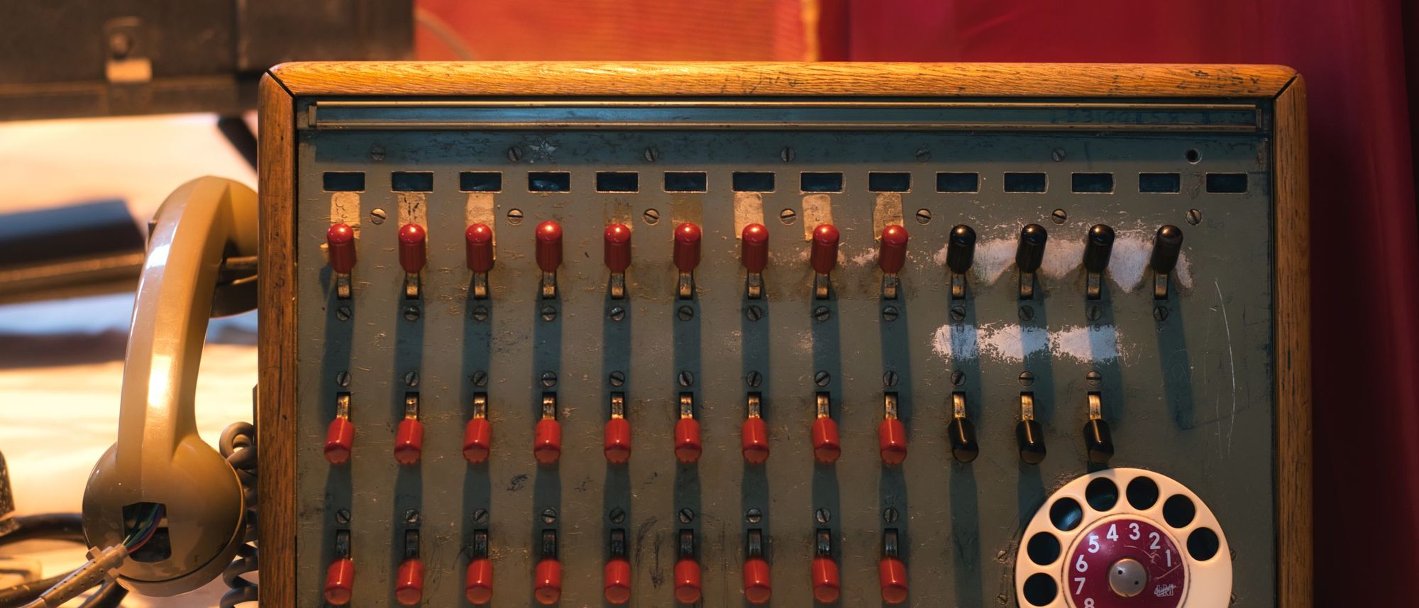 A vintage telephone switchboard with a rotary dial and rows of toggle switches.