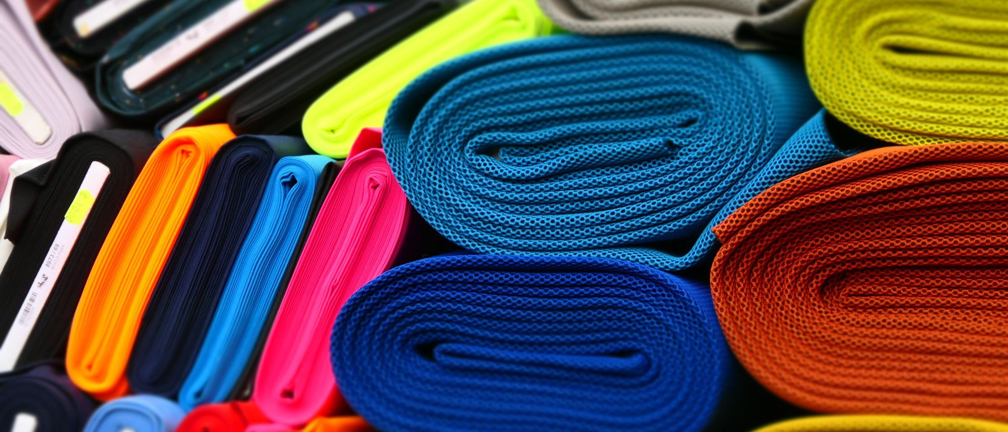 Bolts of brightly coloured fabric are rolled and stacked on the shelves of a textile shop.