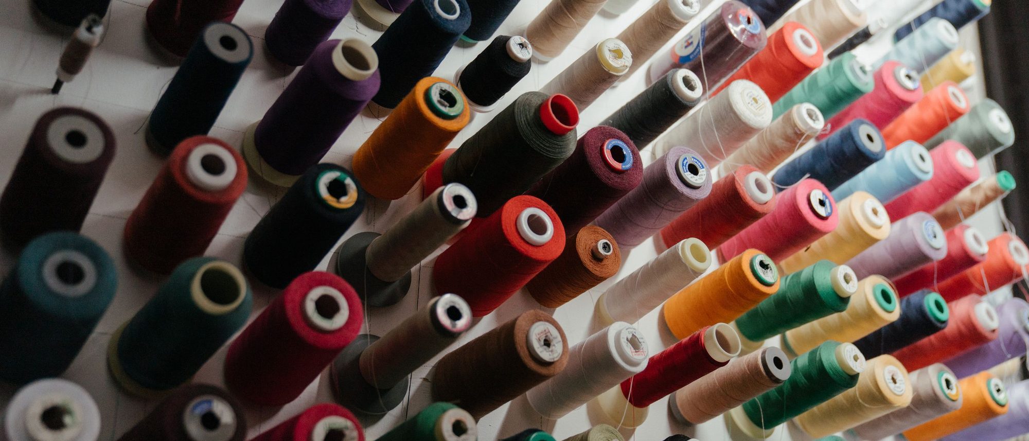 Spools of sewing thread in many colours arranged in rows on a workshop rack.