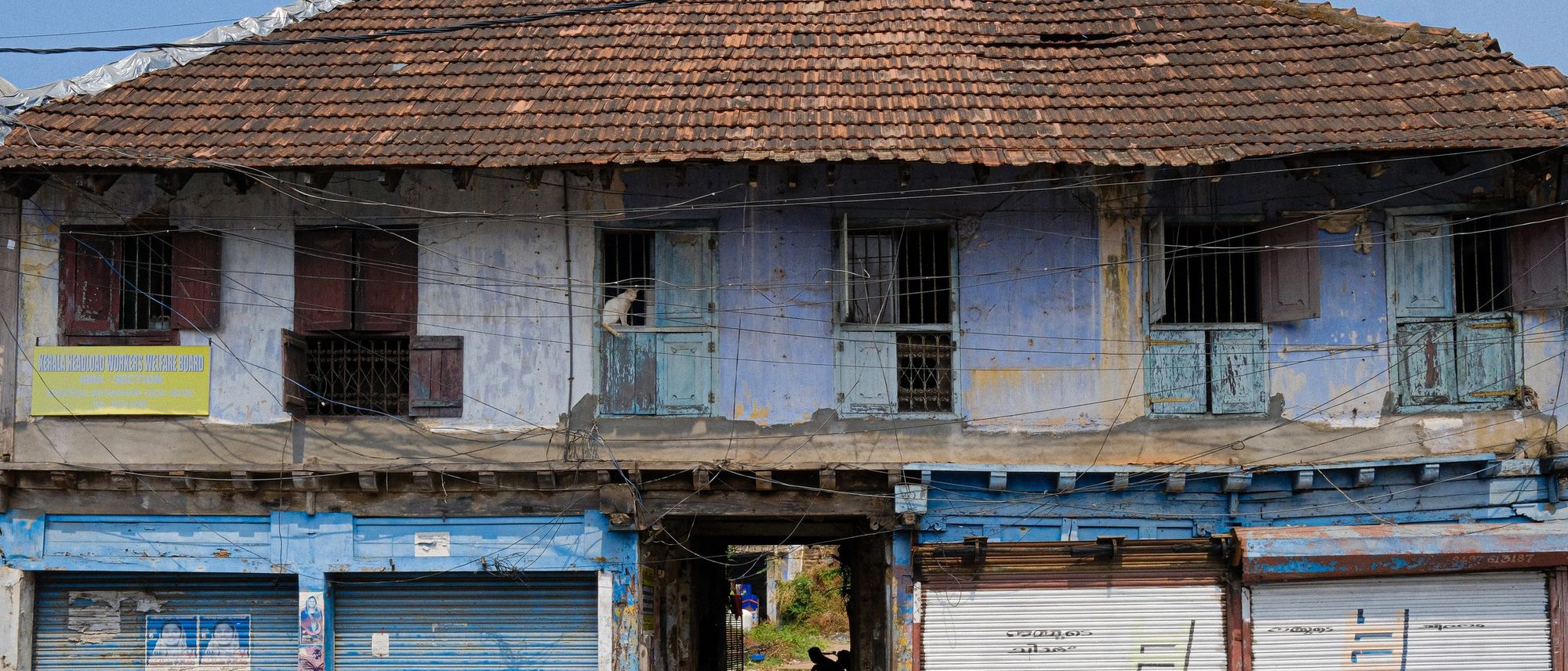 The weathered facade of an old building in Kochi with closed blue shutters.