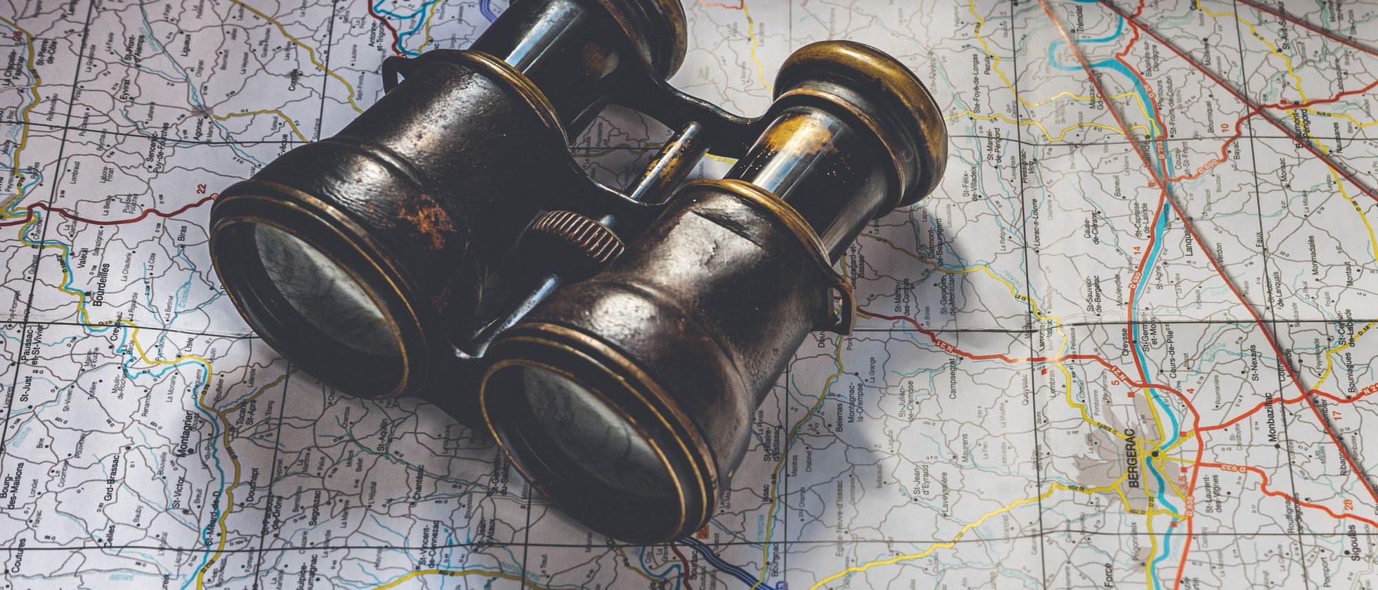 A pair of antique binoculars lying on a detailed road map