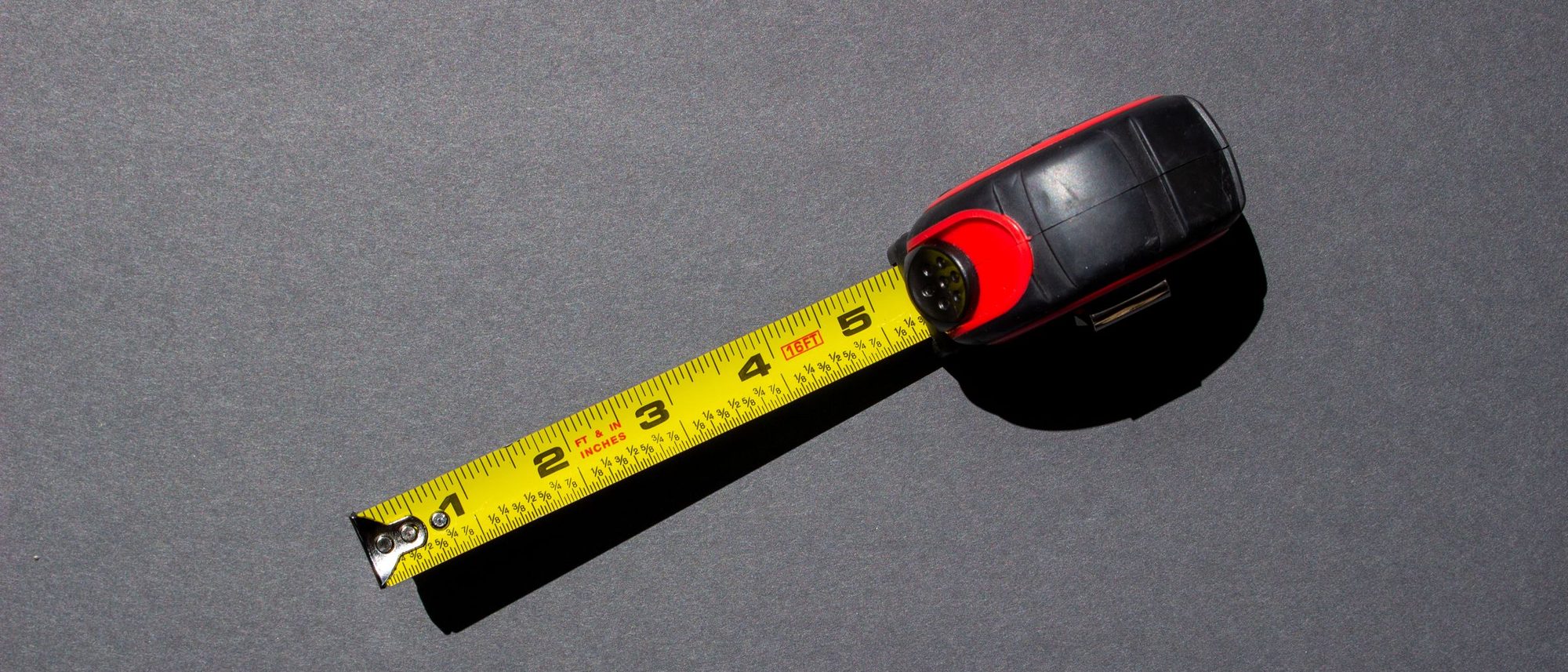 A yellow tape measure lying on a dark surface under bright light.