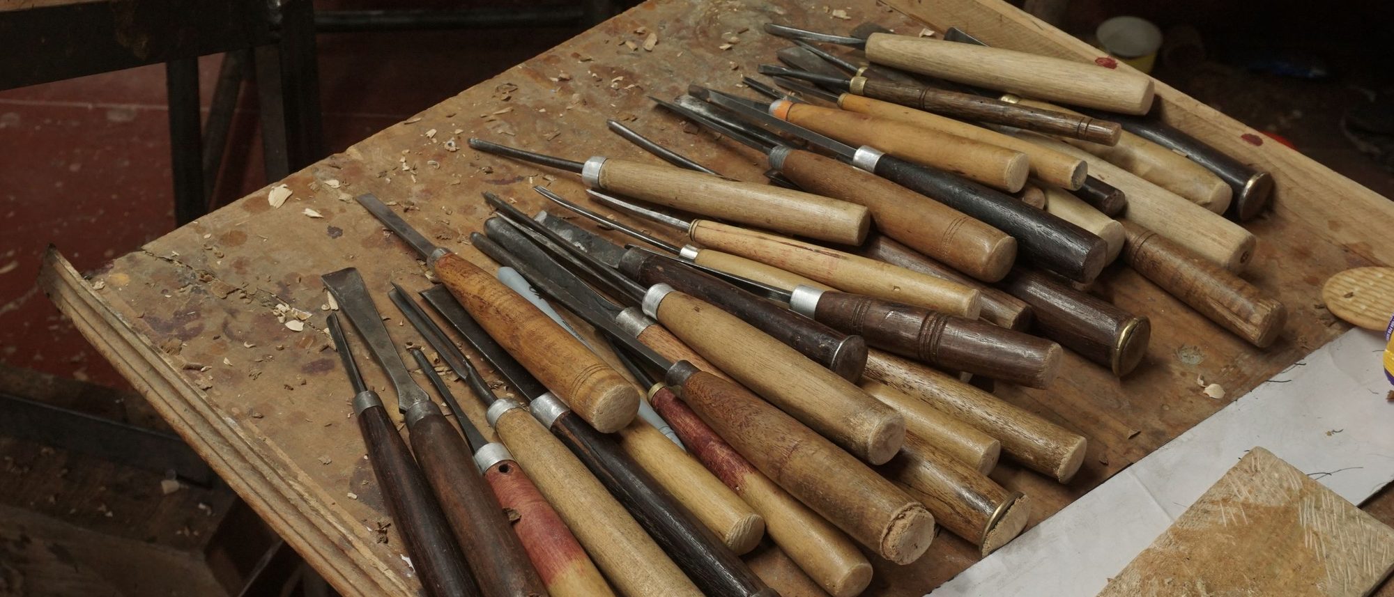 Hand tools for woodturning and carving laid out on a workbench in a Bengaluru workshop.