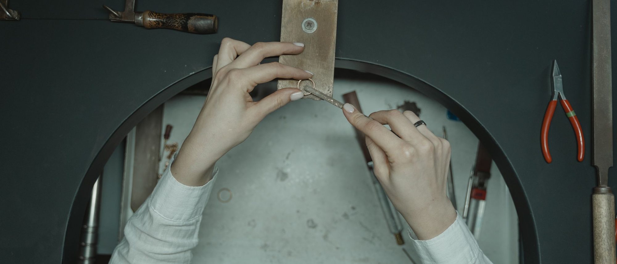 Top-down view of a jeweller’s hands working with small tools on a wooden workbench.