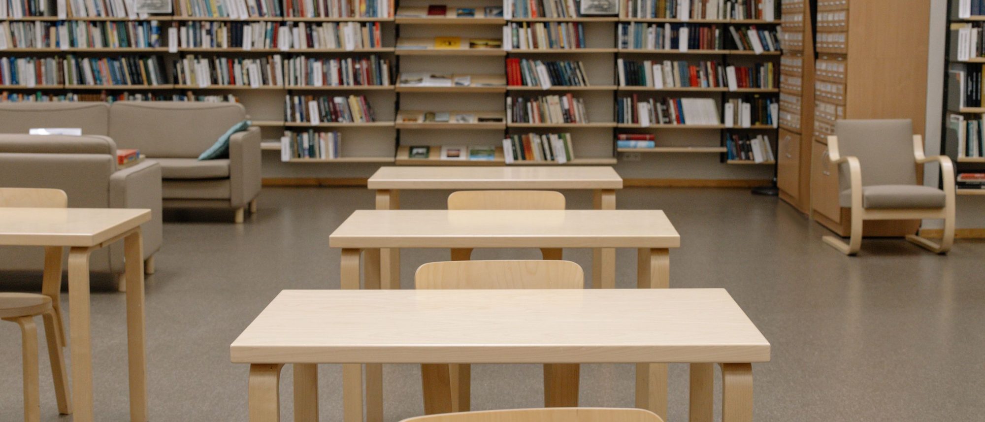 A quiet library with long wooden tables and shelves full of books.