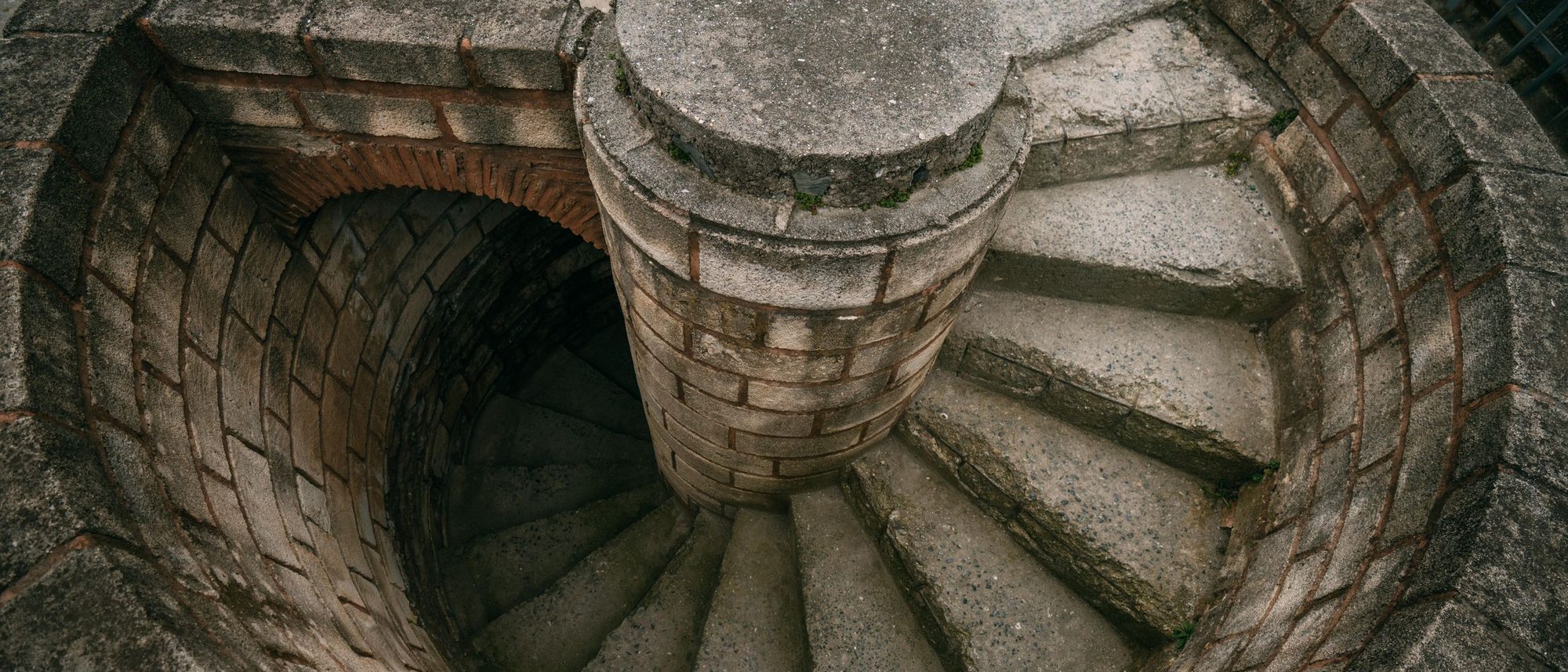 A stone staircase spiralling down around a central column, seen from above.