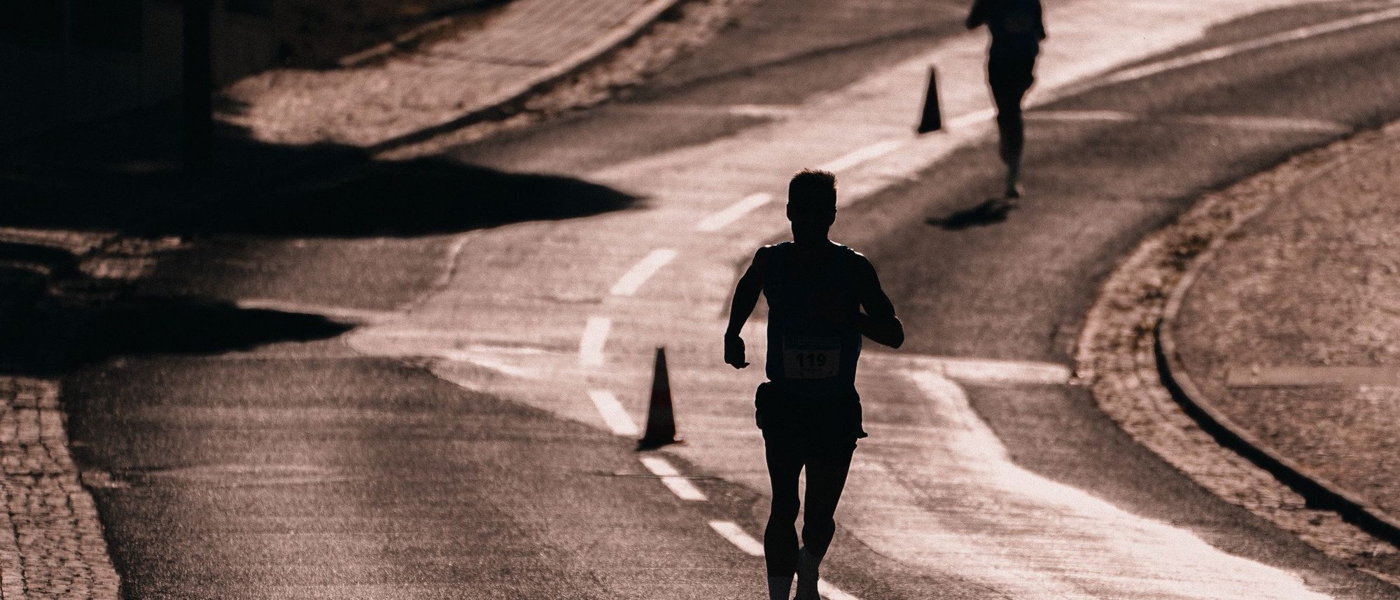 A runner in silhouette moves along a city street during a road race.