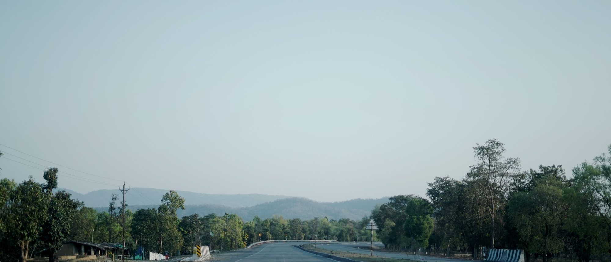 An empty highway running through green countryside near Ambikapur in Chhattisgarh under a clear sky.
