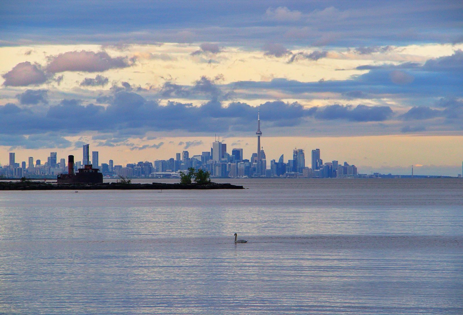 The Toronto skyline and the CN Tower seen across the calm water of Lake Ontario under an evening sky