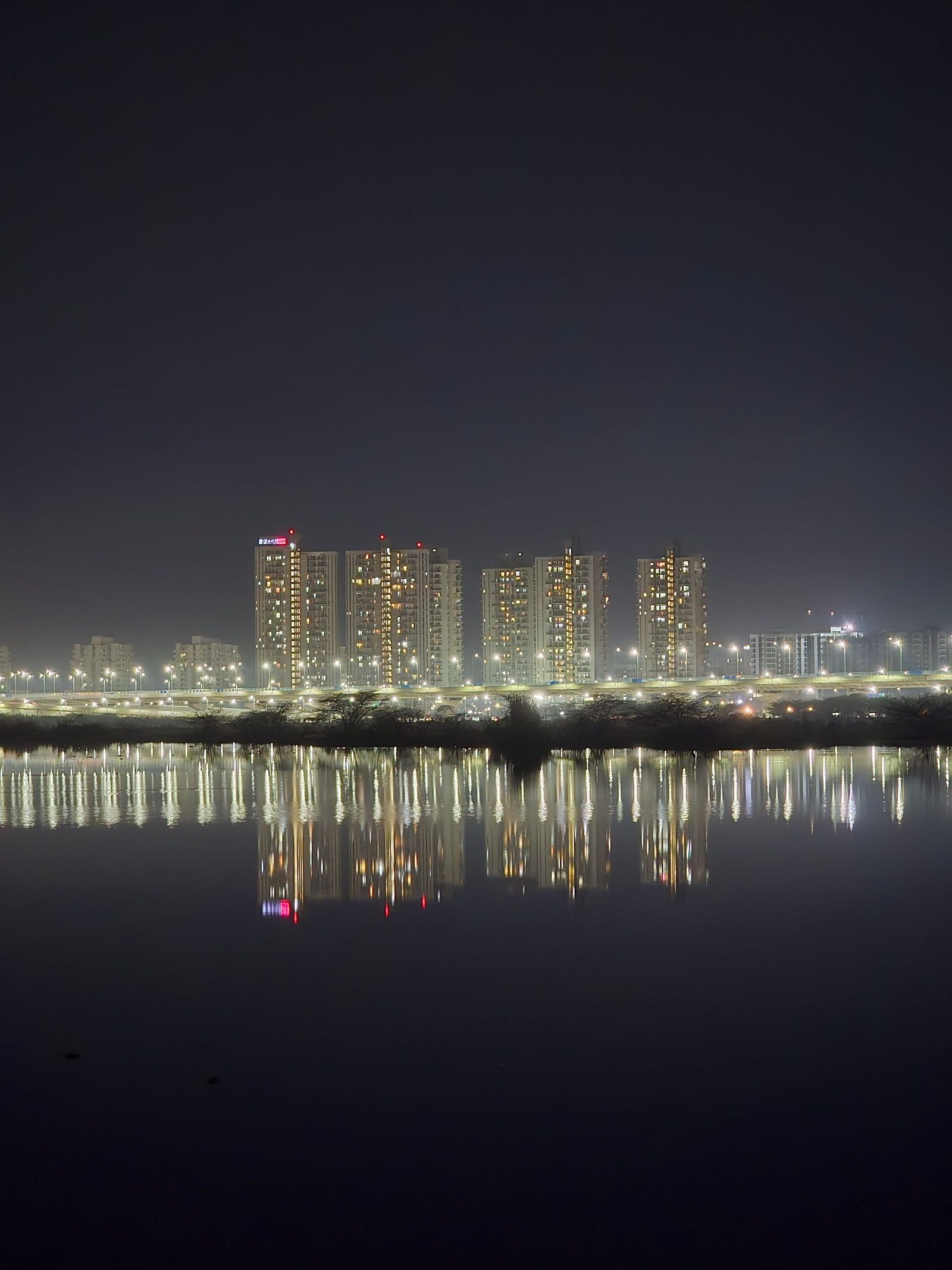 Lit office towers in Gurugram reflected in still water at night.