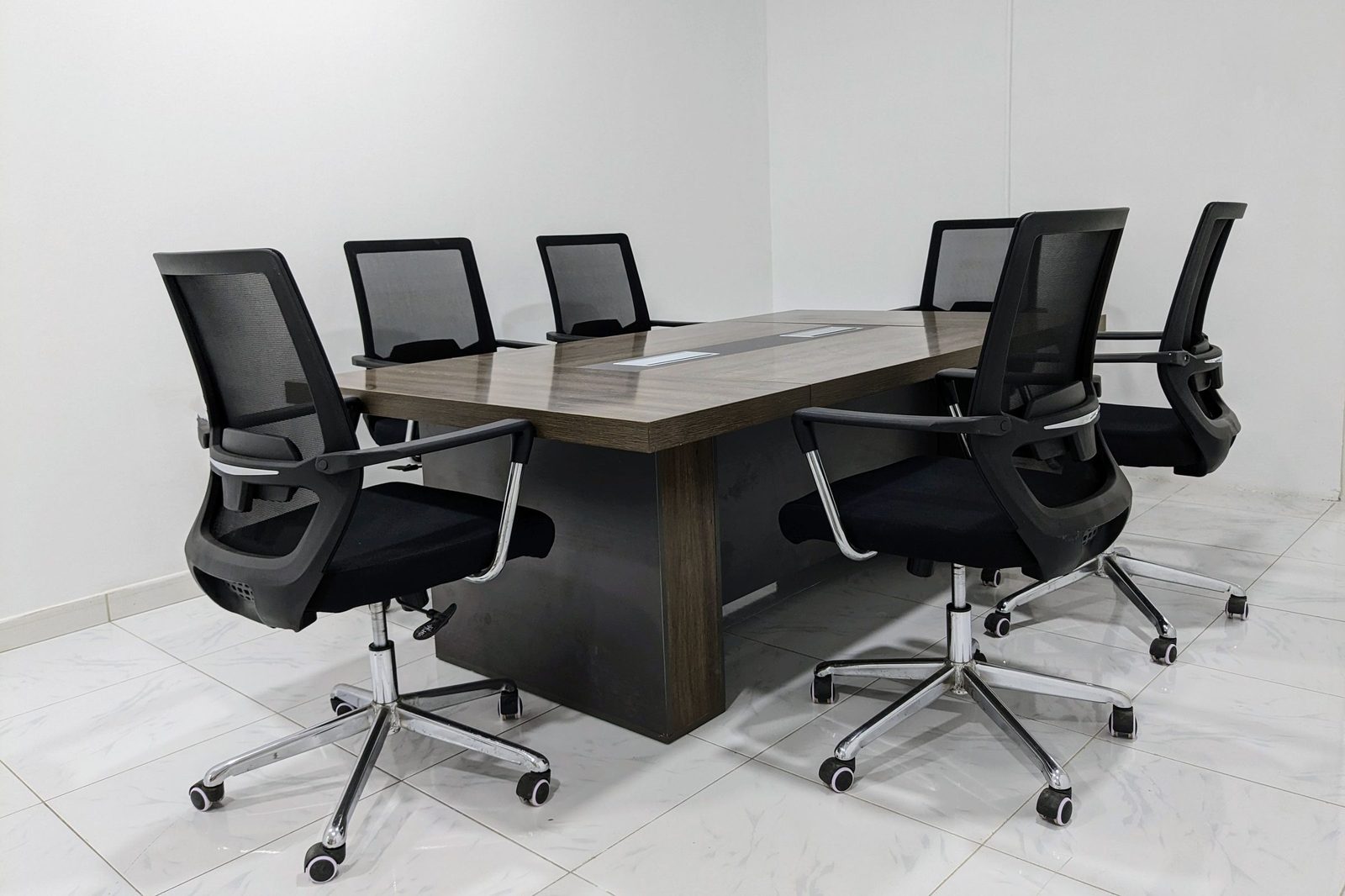 Black mesh chairs around a dark wooden table in a small conference room.