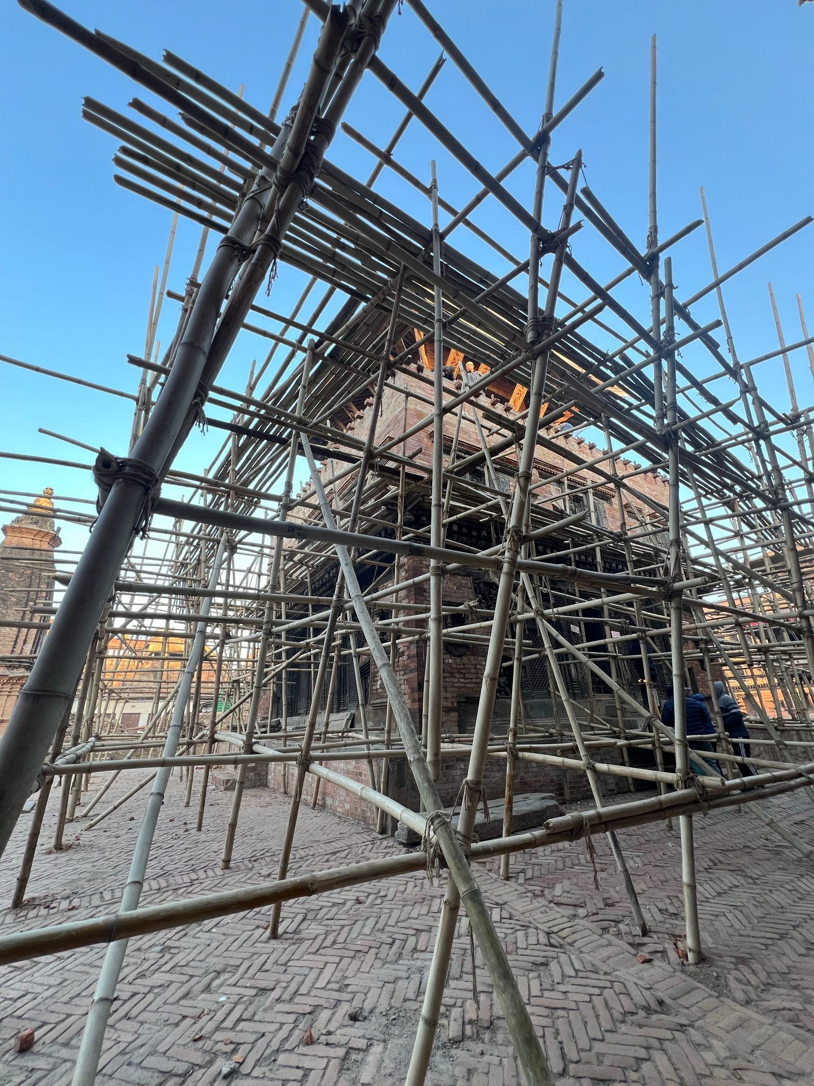 A historic Nepalese temple stands wrapped in bamboo scaffolding during renovation.
