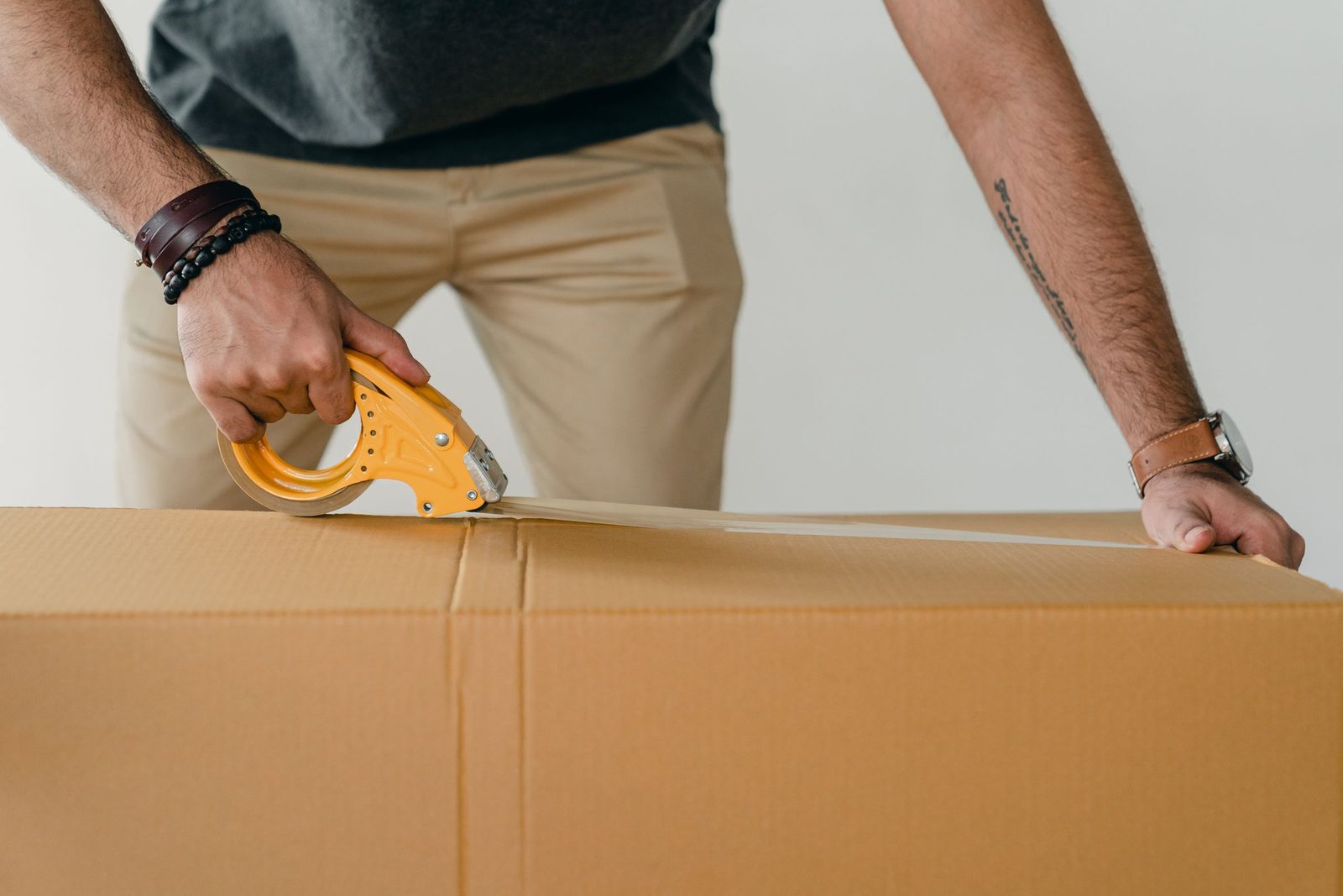 Hands sealing a cardboard carton with a tape dispenser.