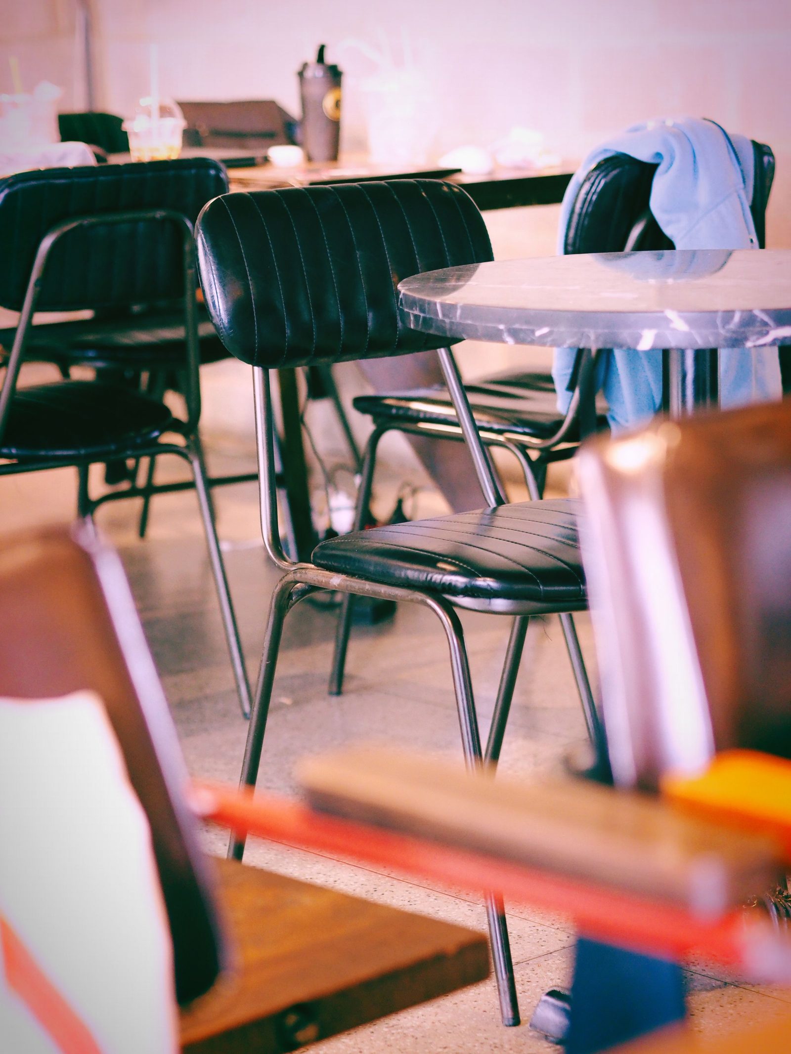 A warmly lit vintage café with black chairs and tables and nobody seated.