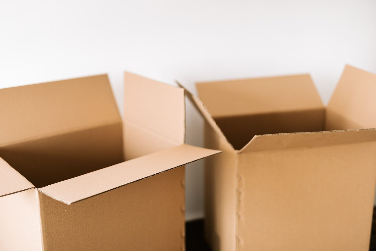 Two open cardboard boxes on a dark surface against a white wall in daylight.
