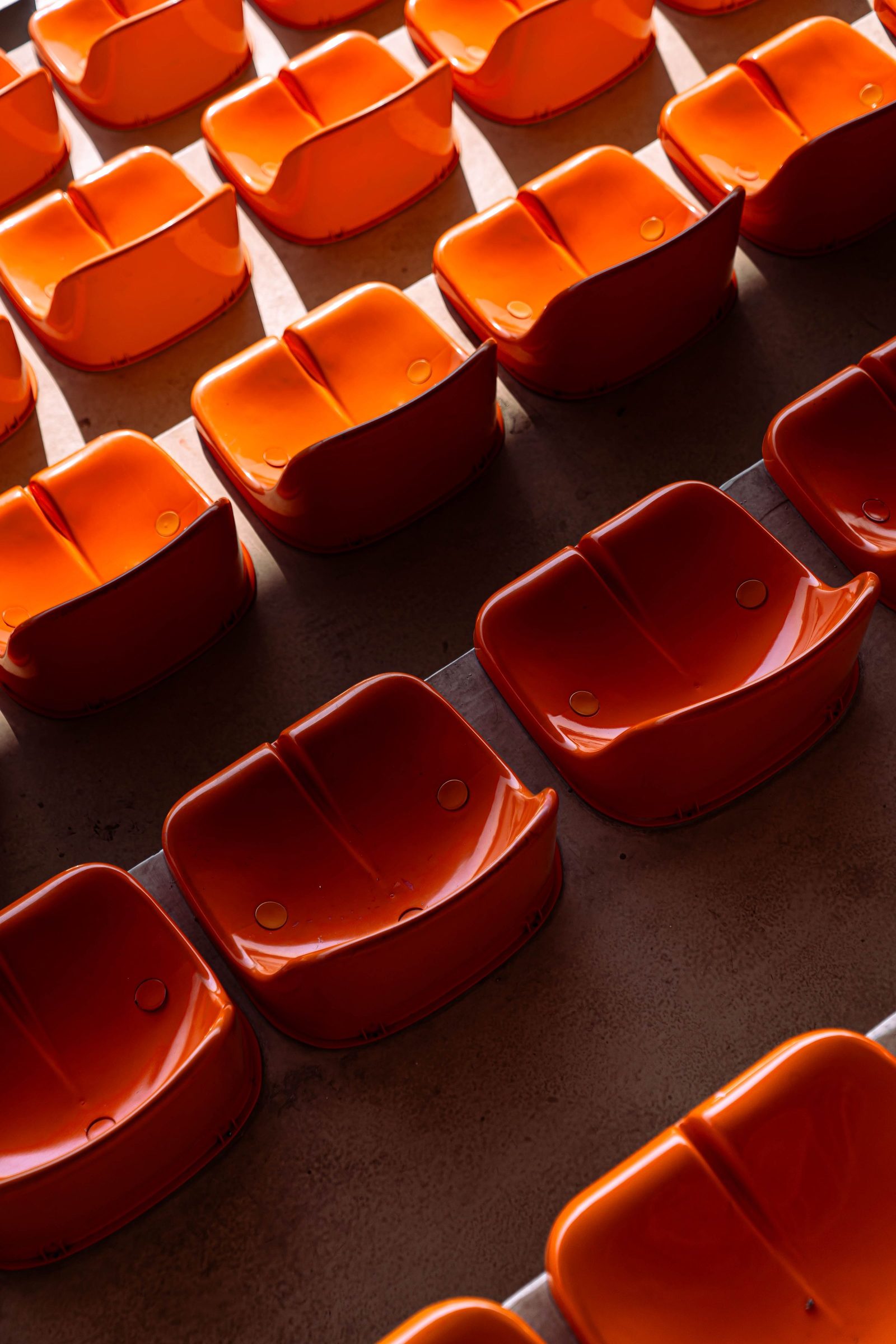 Rows of orange plastic stadium seats repeat in sunlight.