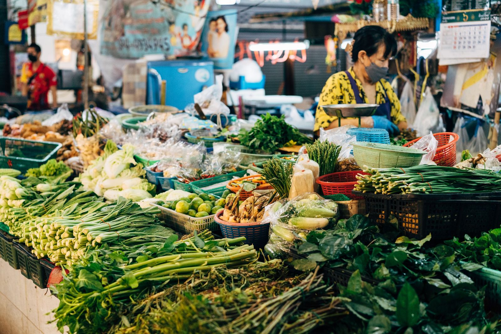 A vendor at a crowded market stall stacked with fresh vegetables.