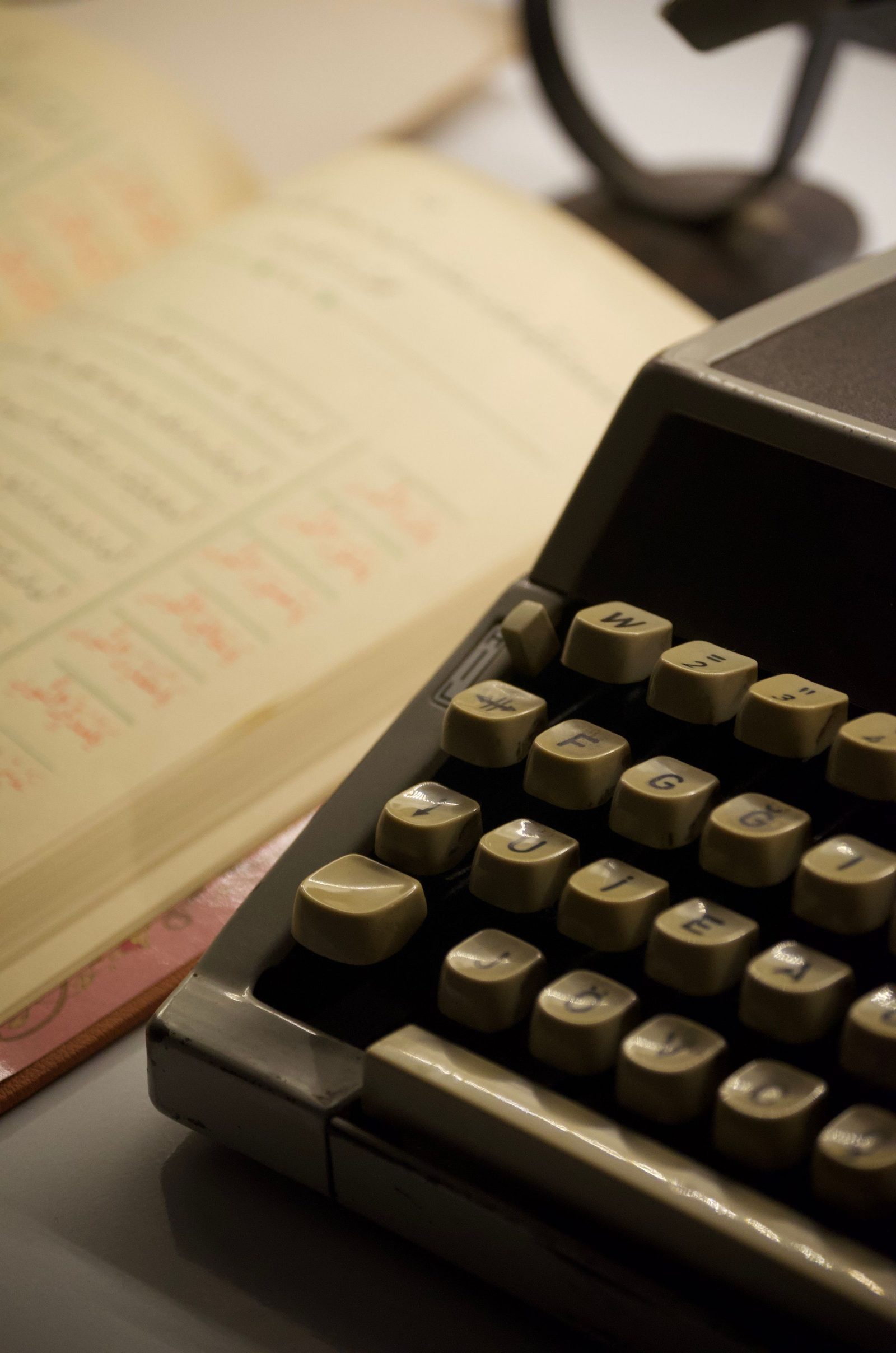 An old typewriter sits beside an open handwritten ledger on a desk.