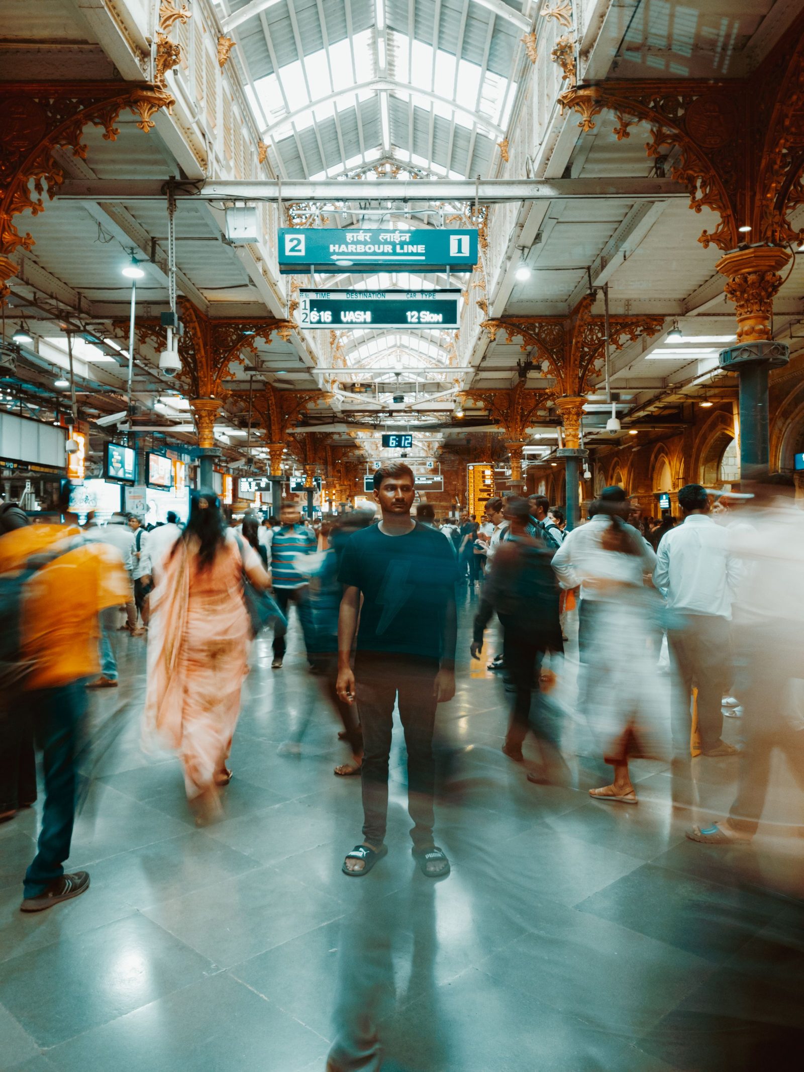 A long exposure of a busy Mumbai station with commuters blurred as they pass one figure standing still.