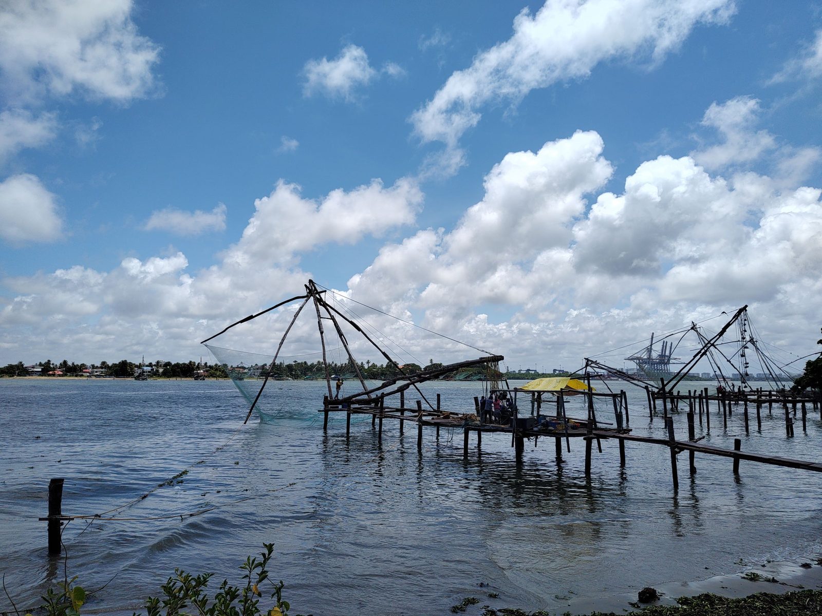 The timber frames of Chinese fishing nets stand over the water at Fort Kochi under a blue sky.