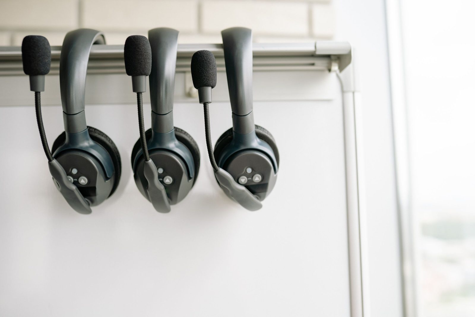 Three black headsets hanging from a hook on a whiteboard.