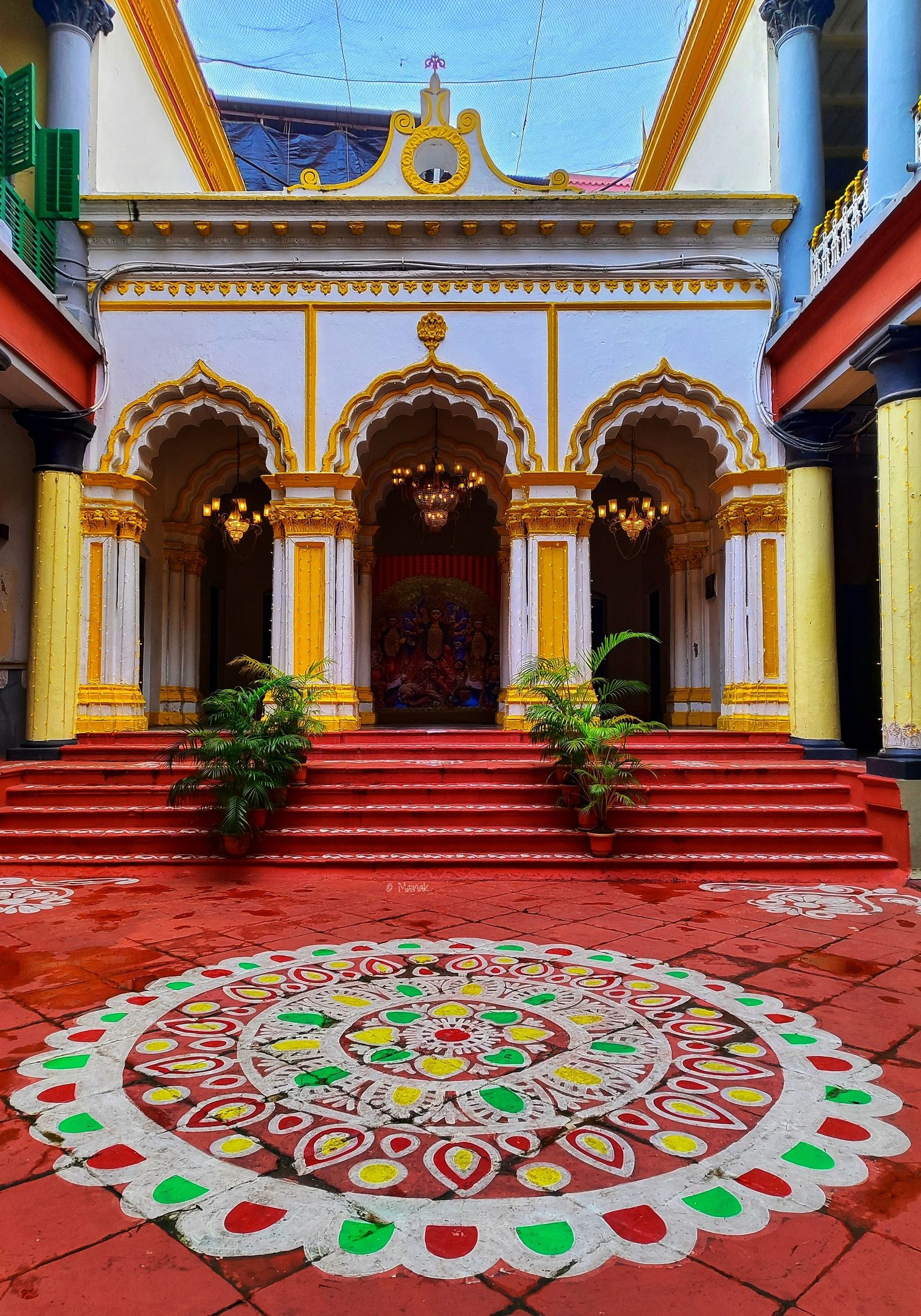 A kolam drawn on the floor of a courtyard in front of an ornate doorway.