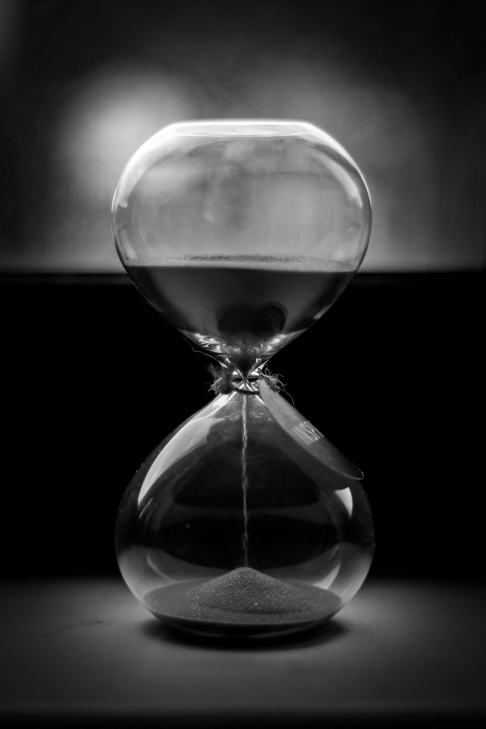 A black-and-white close-up of sand running through an hourglass.