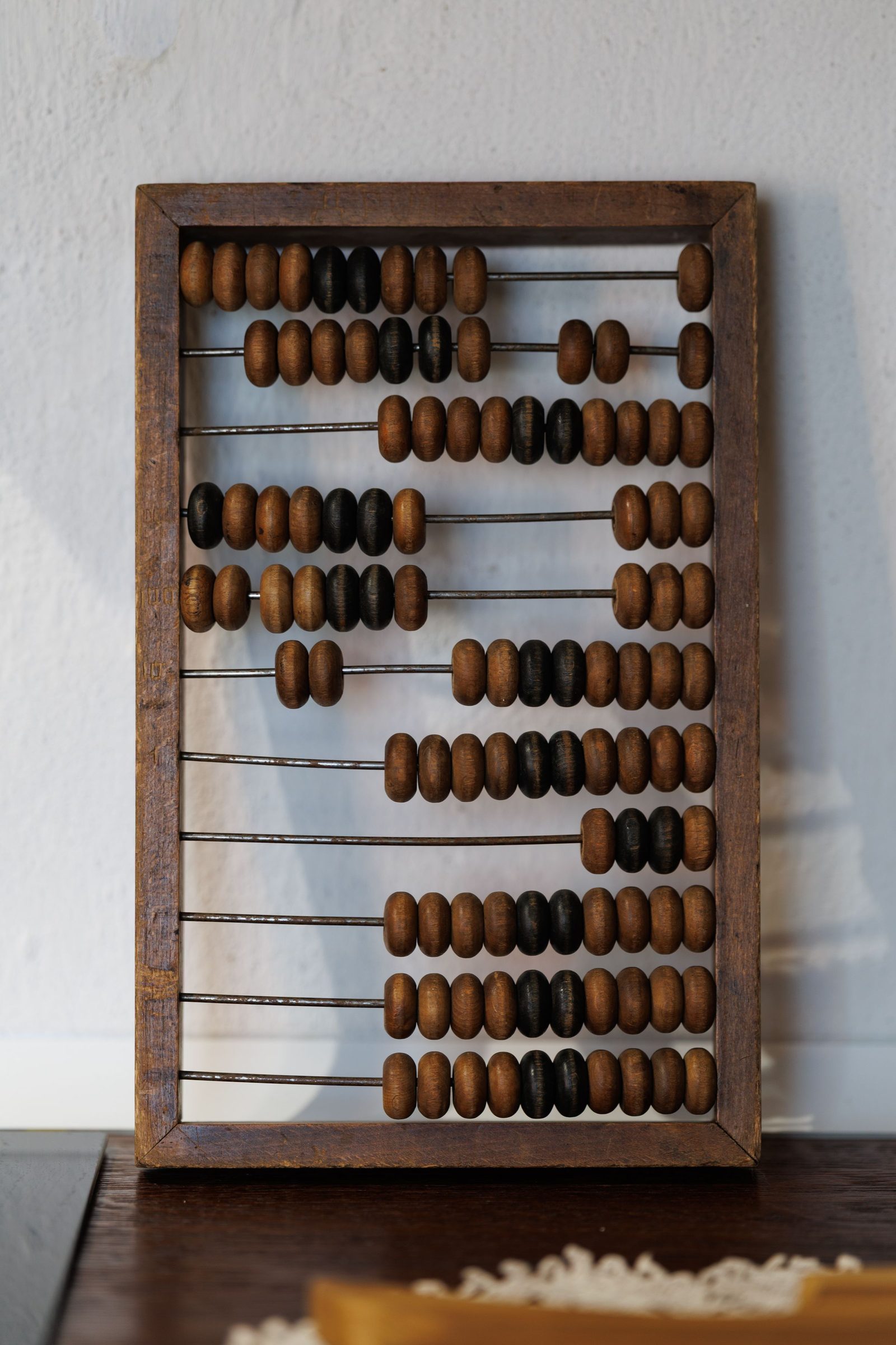 A vintage wooden abacus with brown and black beads against a white wall.
