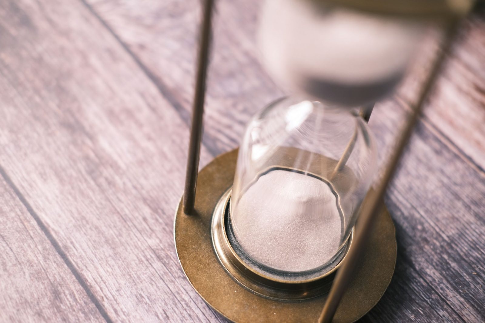 A glass hourglass with white sand stands on a brown wooden table.