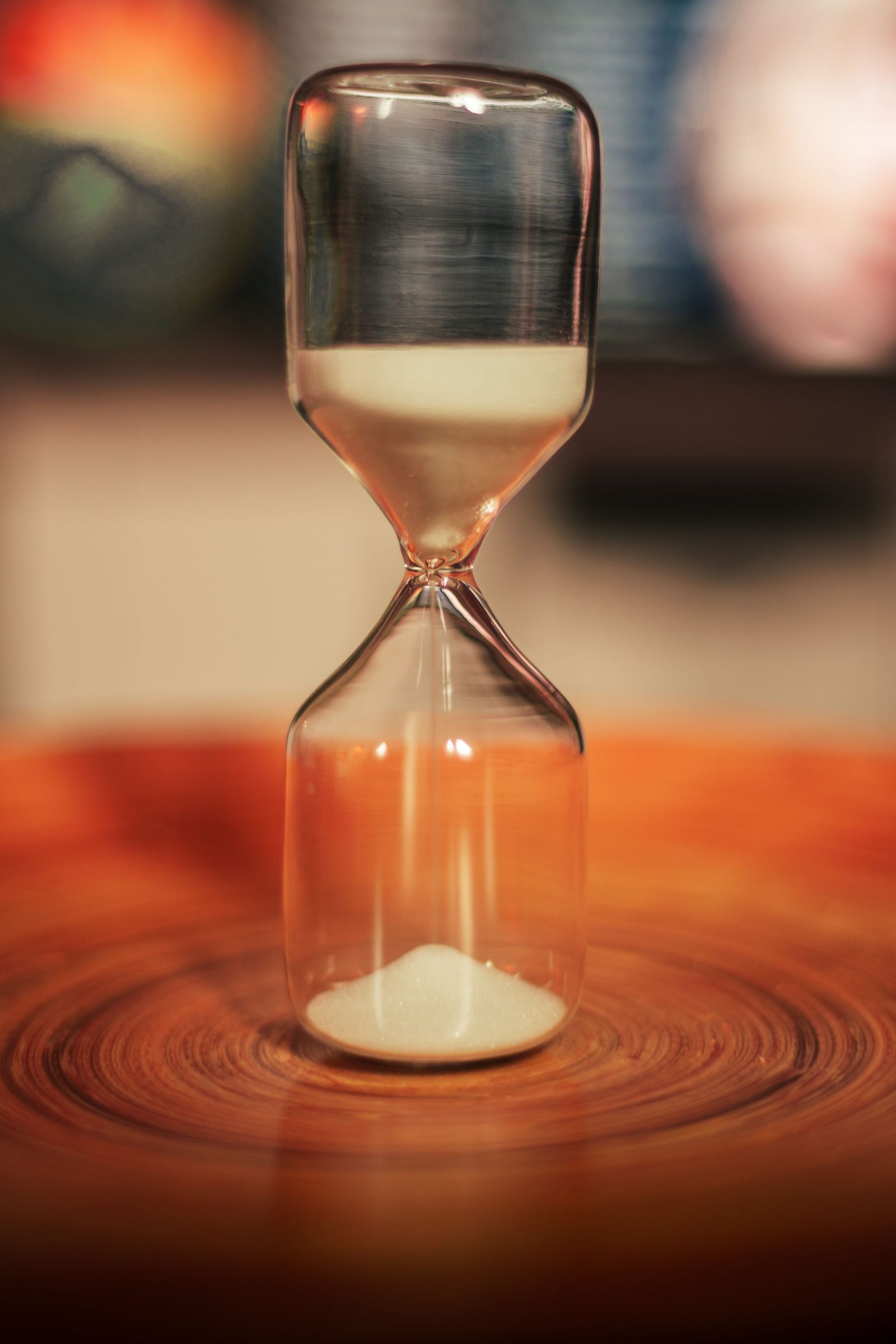 A clear glass hourglass with sand running through it on a wooden surface.