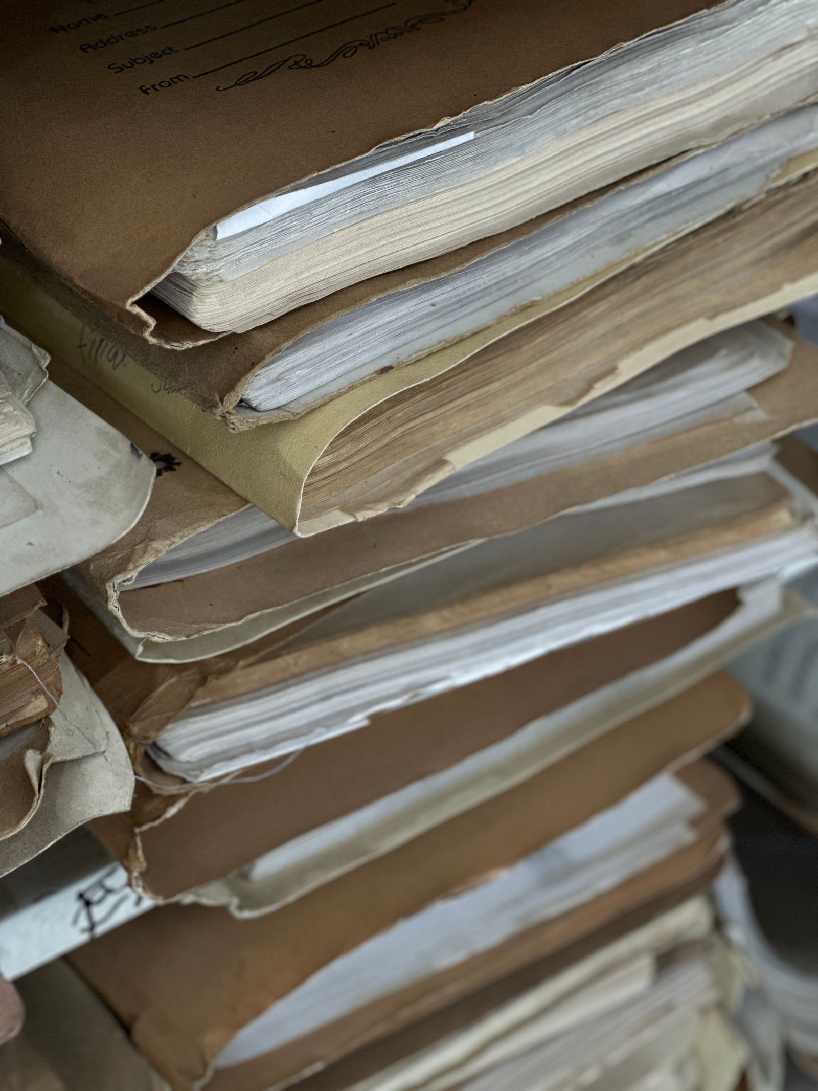 A stack of old paper files in brown folders tied and piled on a shelf.